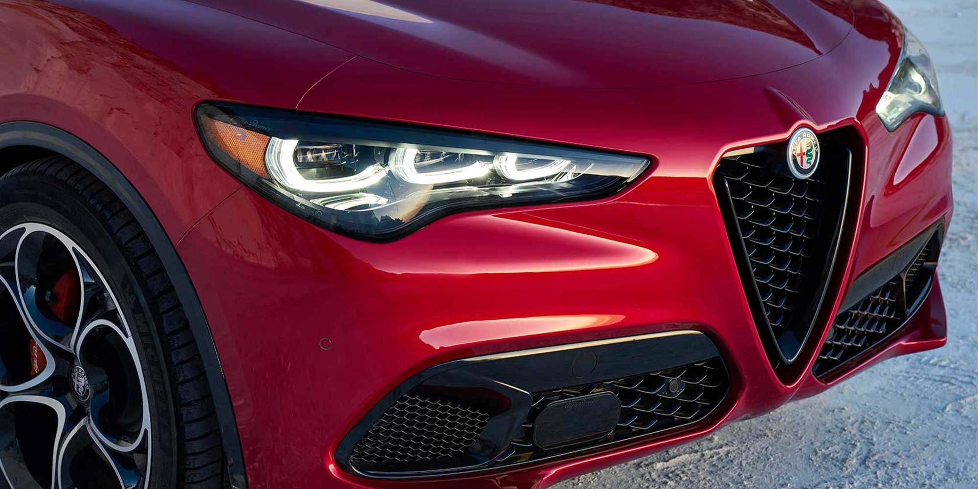 Close-up of the red 2026 Alfa Romeo Stelvio’s front corner, highlighting the sleek headlight design and grille.