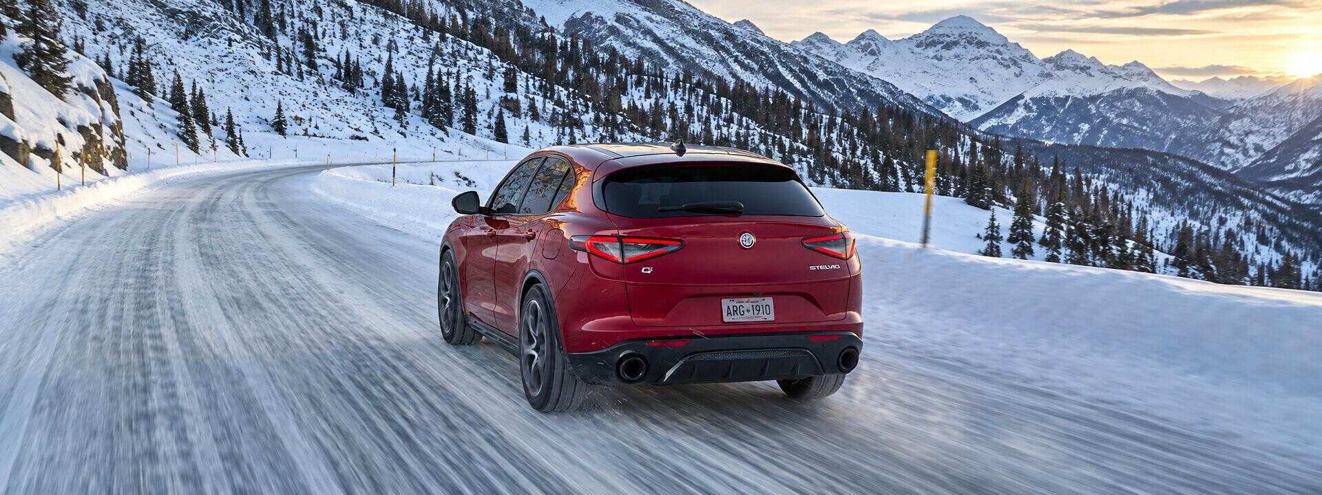 Rear view of the 2026 Alfa Romeo Stelvio in motion on a snow-covered road, showcasing its sleek taillights and sporty design.