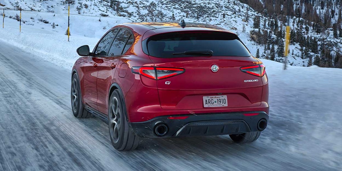 Rear view of the 2026 Alfa Romeo Stelvio in motion on a snow-covered road, showcasing its sleek taillights and sporty design.