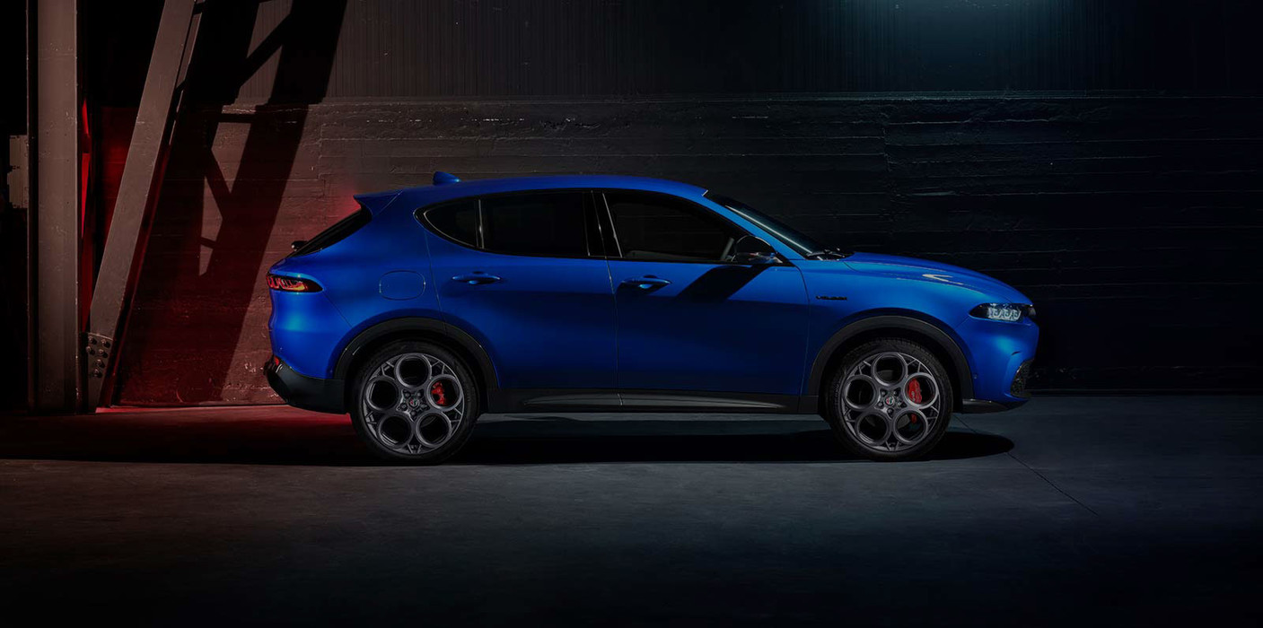 Alfa Romeo Tonale 2025 bleu Misano métallisé est stationné à l’intérieur, dans un cadre moderne et industriel, avec une lumière vive au-dessus de la tête.