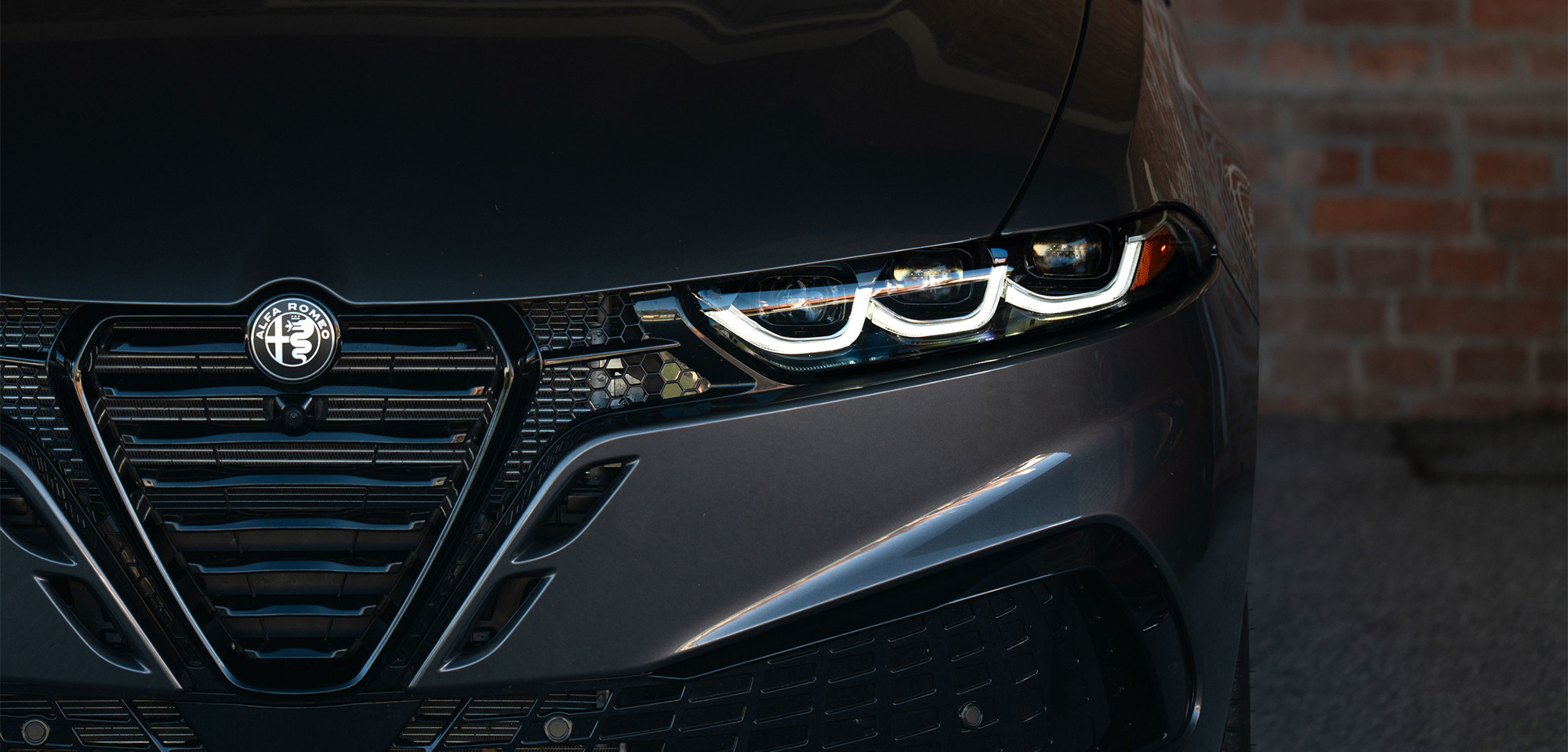 Gros plan sur un Alfa Romeo Tonale à essence noir 2026, mettant en valeur le design élégant des phares, partiellement encadrés par un mur de briques, soulignant son style moderne et audacieux.