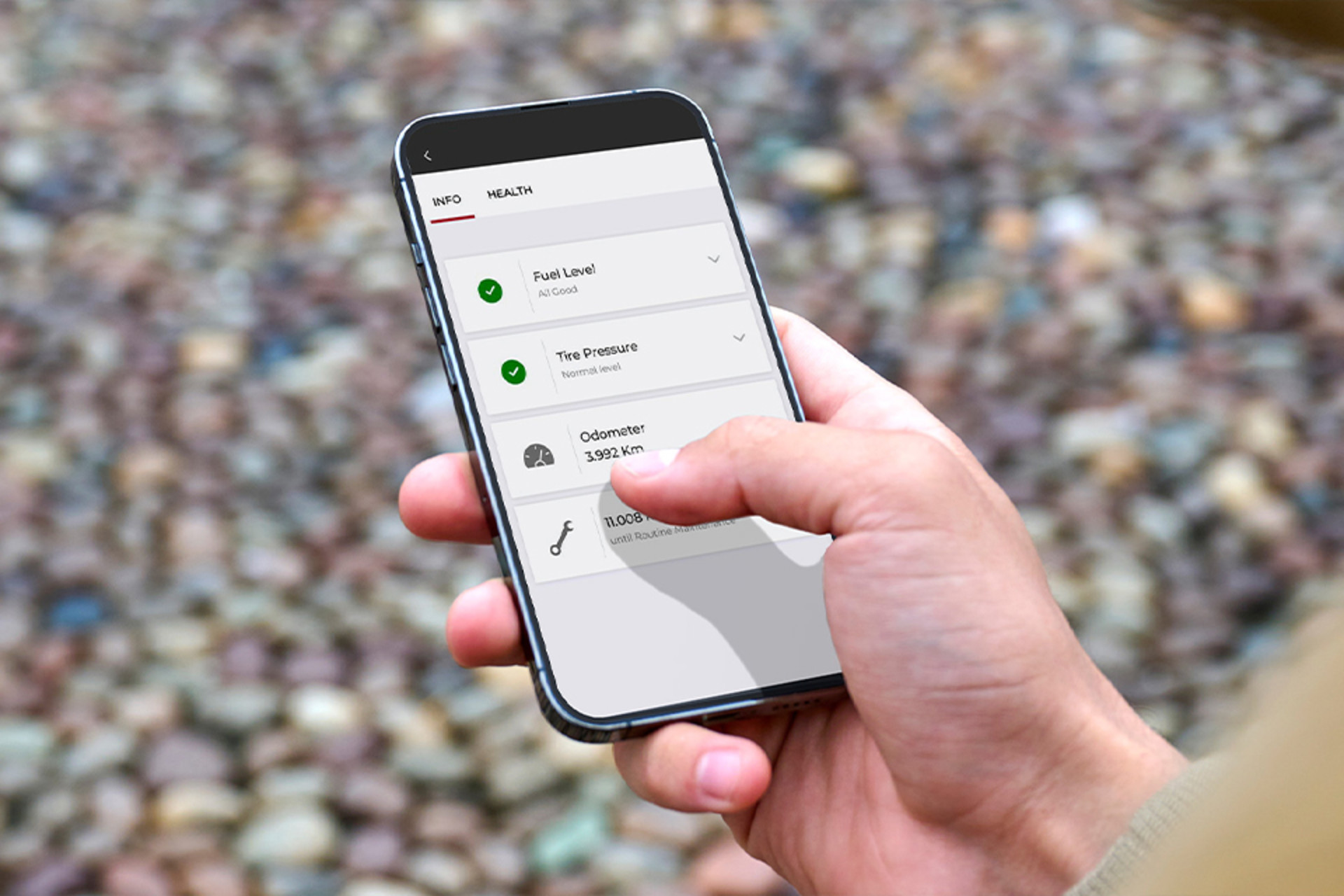 Une personne tenant un téléphone intelligent affichant une application de diagnostic véhicule, avec des options pour le niveau de carburant, la pression des pneus et le compteur kilométrique, témoignant de fonctionnalités de connectivité modernes.
