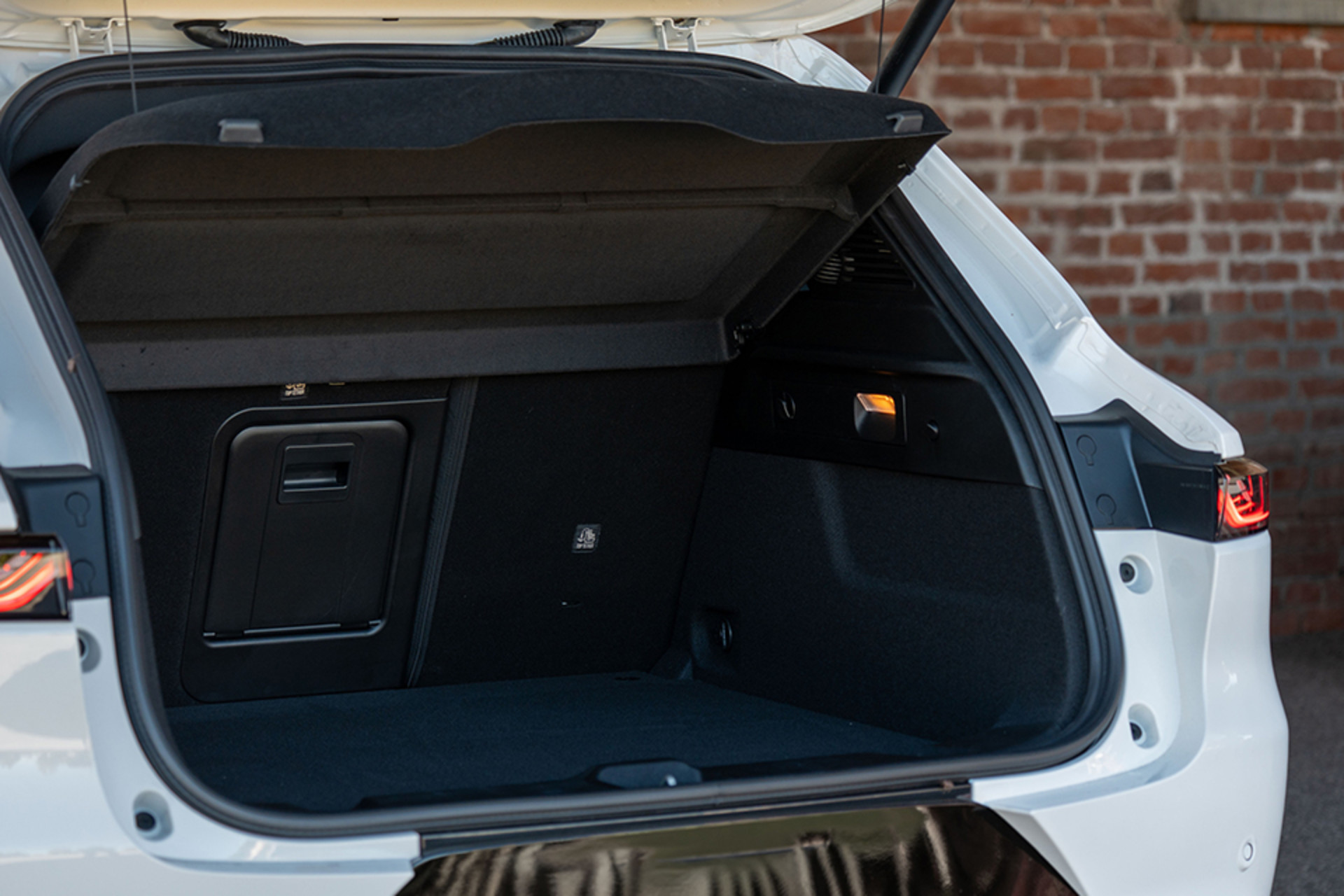 Un Alfa Romeo Tonale à essence blanc 2026 avec un coffre ouvert, mettant en valeur un espace de chargement spacieux et un design élégant et pratique sur fond de mur de briques.