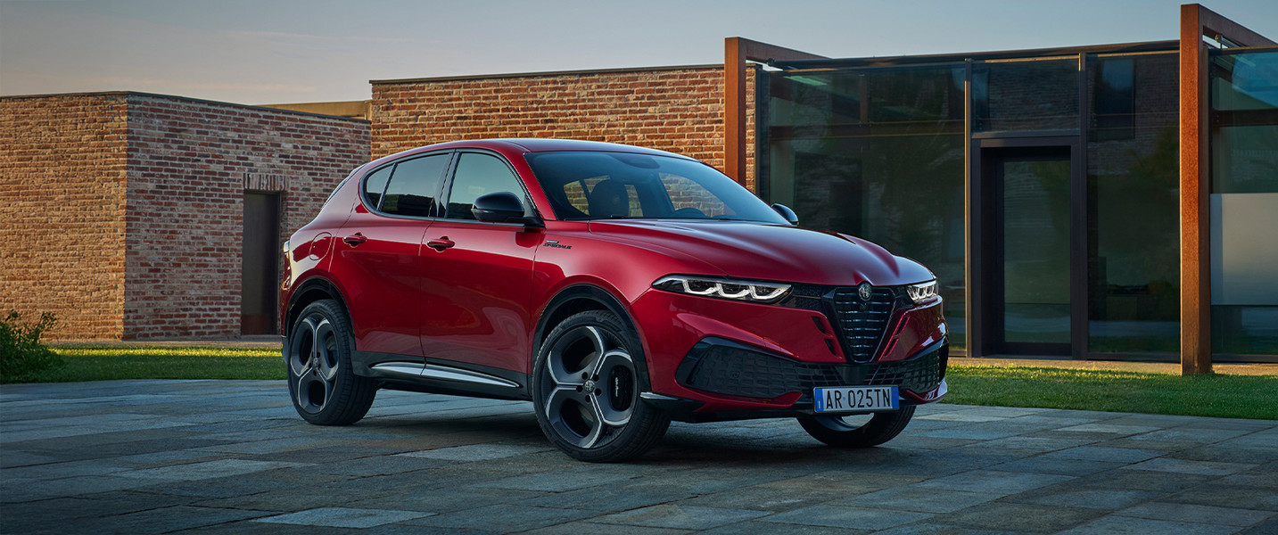 Un Alfa Romeo Tonale à essence rouge 2026, garé dans une cour moderne, met en valeur son design élégant et ses courbes stylisées sur un fond architectural contemporain.