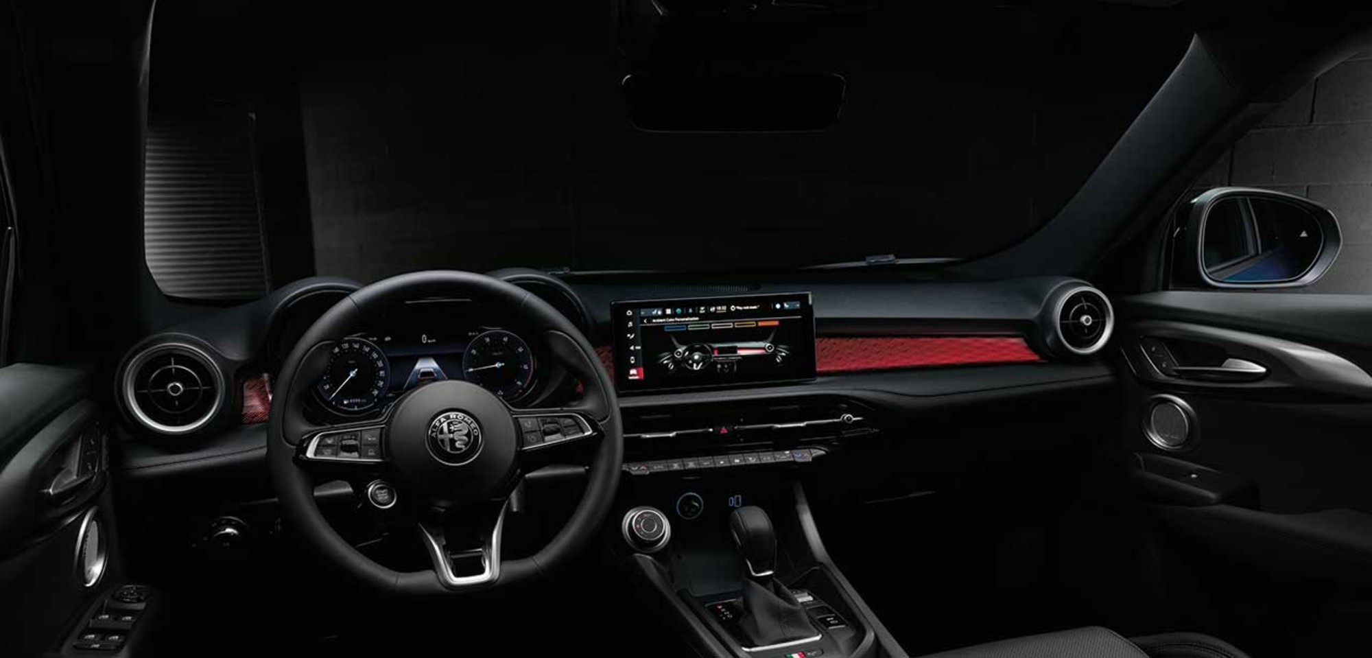 Intérieur d'un Alfa Romeo Tonale VHR 2025 présentant le tableau de bord, le volant et le système d'infodivertissement avec un éclairage d'accentuation rouge.