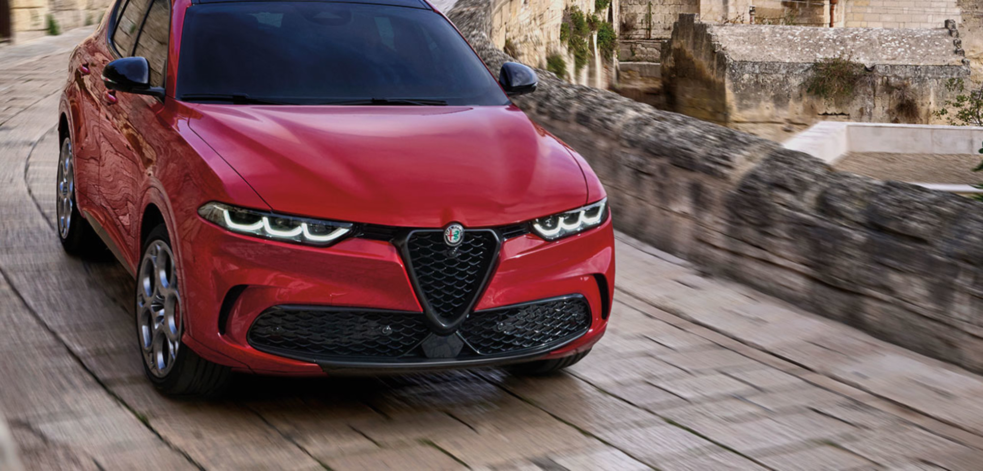Vue de face d'un Alfa Romeo Tonale VHR de couleur bleu Misano métallisé 2025, mettant en valeur sa calandre élégante et ses phares distinctifs dans un cadre faiblement éclairé.