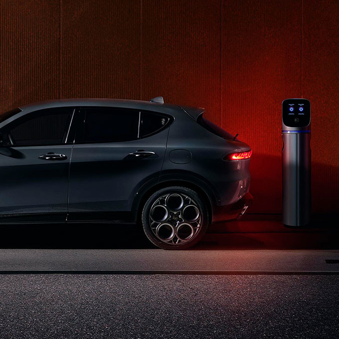 Side view of a Grigio Ascari Metallic 2025 Alfa Romeo Tonale PHEV parked next to a charging station.