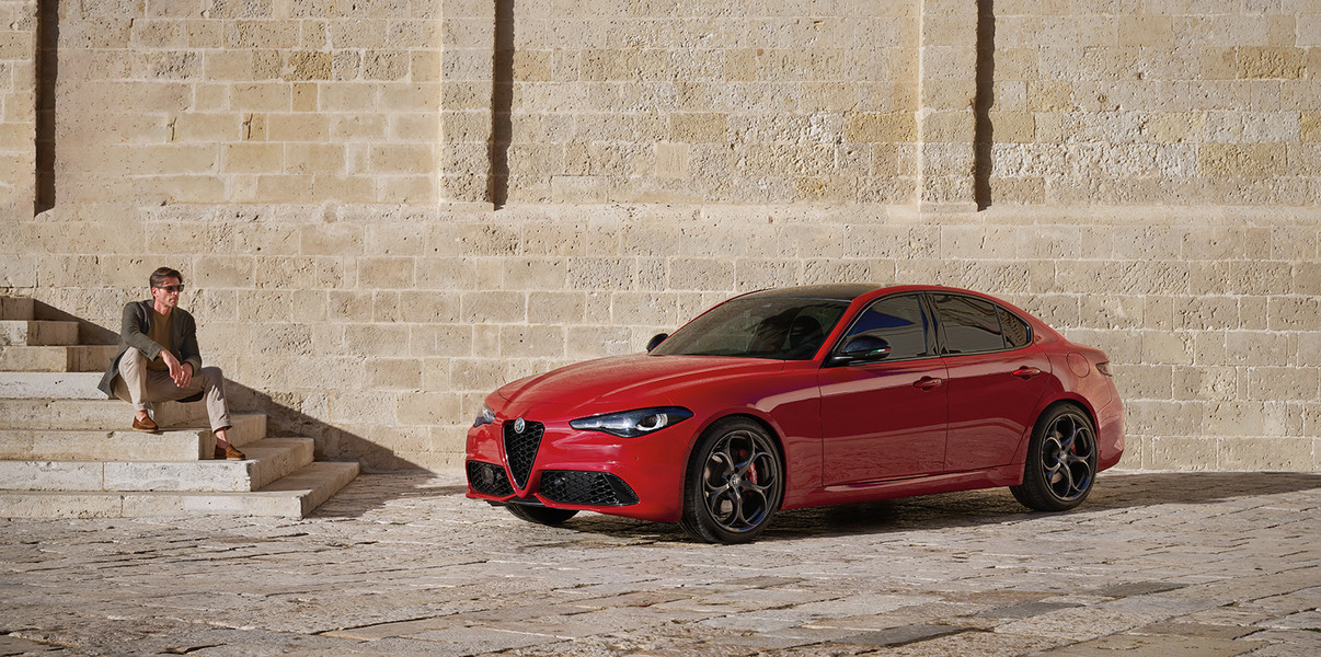 Alfa Romeo Stelvio Tributo Italiano 2025 de couleur Alfa Rosso stationné devant une maison moderne, avec une personne debout à côté.