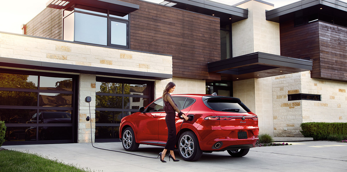 Alfa Romeo Stelvio Tributo Italiano 2025 de couleur Alfa Rosso stationné devant une maison moderne, avec une personne debout à côté.