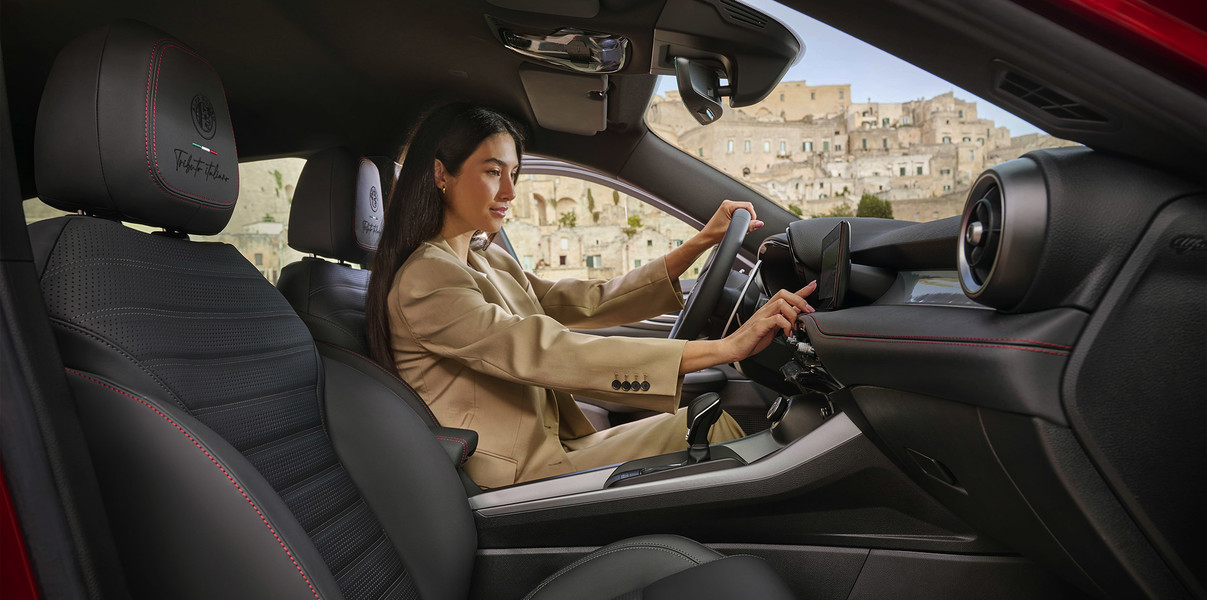 Vue de l’intérieur, d’une personne au volant de l’Alfa Romeo Tonale Tributo Italiano 2025 qui touche son système d’infodivertissement tout en tenant le volant.