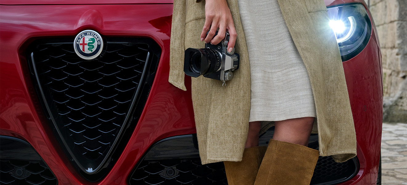  Vue avant d’un véhicule Alfa Romeo Tributo Italiano 2025 avec une personne vêtue d’un manteau tenant un appareil photo devant le véhicule.