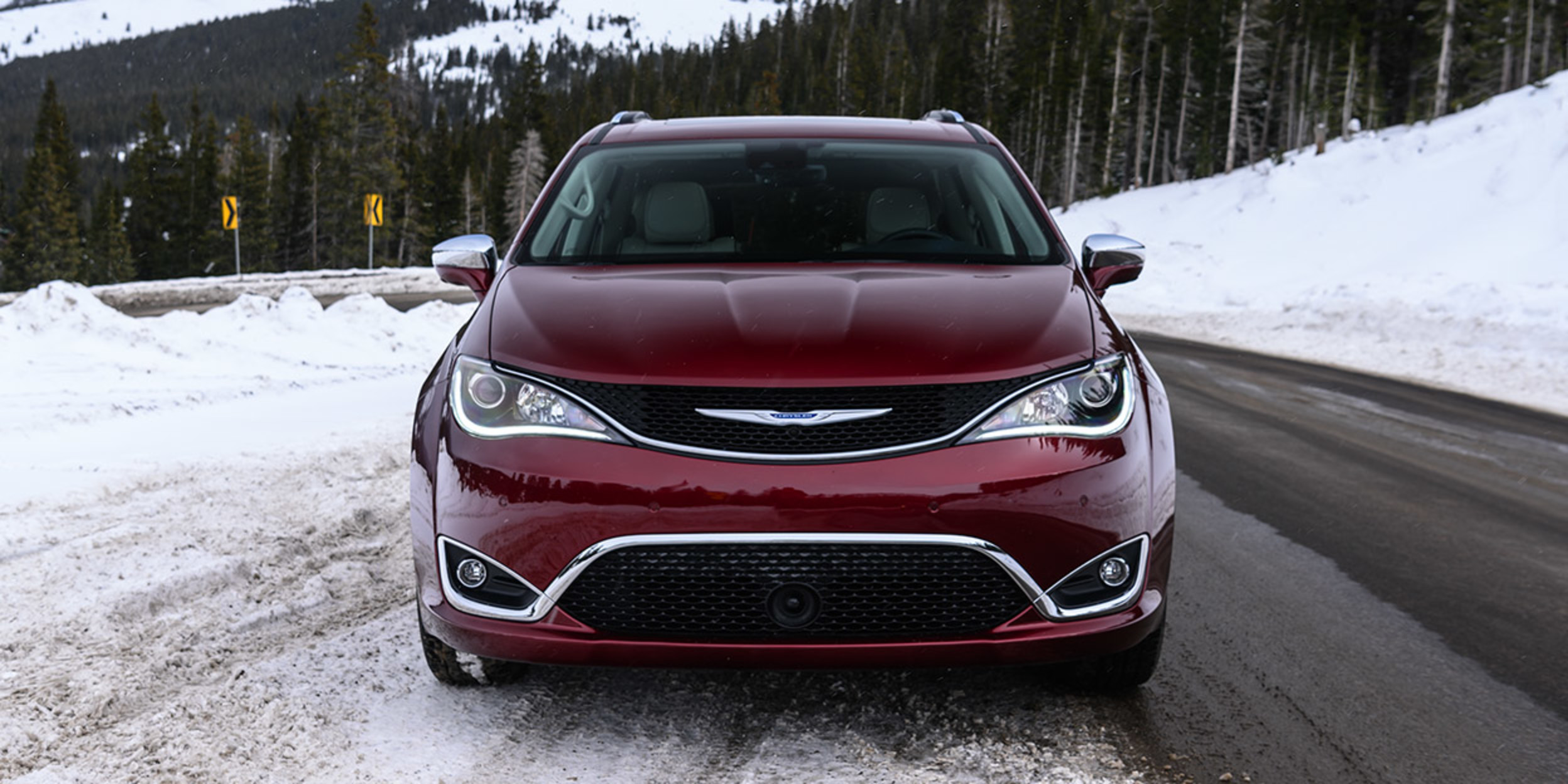 Rear three quarter view of Red Chrysler Pacifica parked at a beach beside two people standing toward the sea
