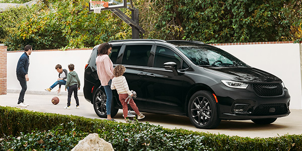 Une Chrysler Pacifica noire stationnée dans une entrée où une mère et sa fille utilisent le mécanisme mains libres pour ouvrir les portes latérales.