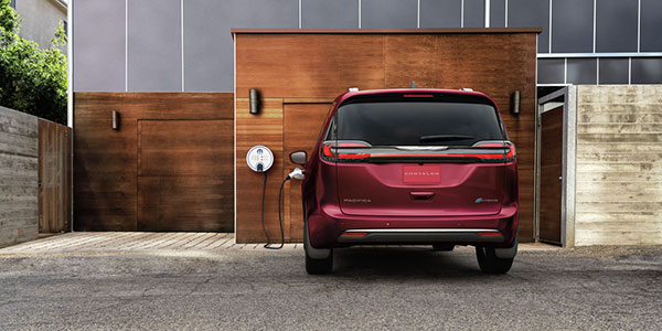 Back view of a red 2023 Chrysler Pacifica Hybrid PHEV parked at an electric charging station outside.