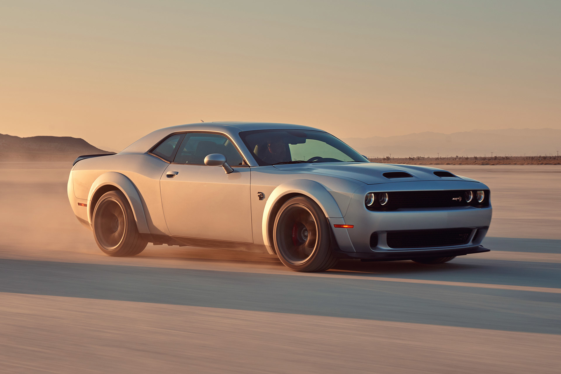 A silver 2022 Dodge Challenger being driven through a desert plain, kicking up dust.
