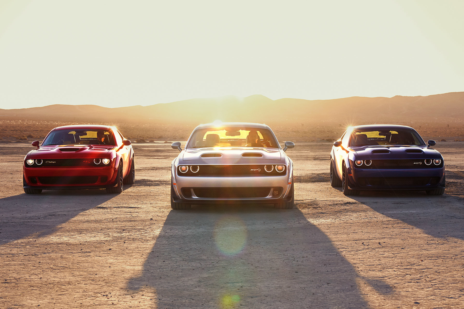 Red, silver, and black 2022 Dodge Challengers, all parked on a desert field with mountains in the background.