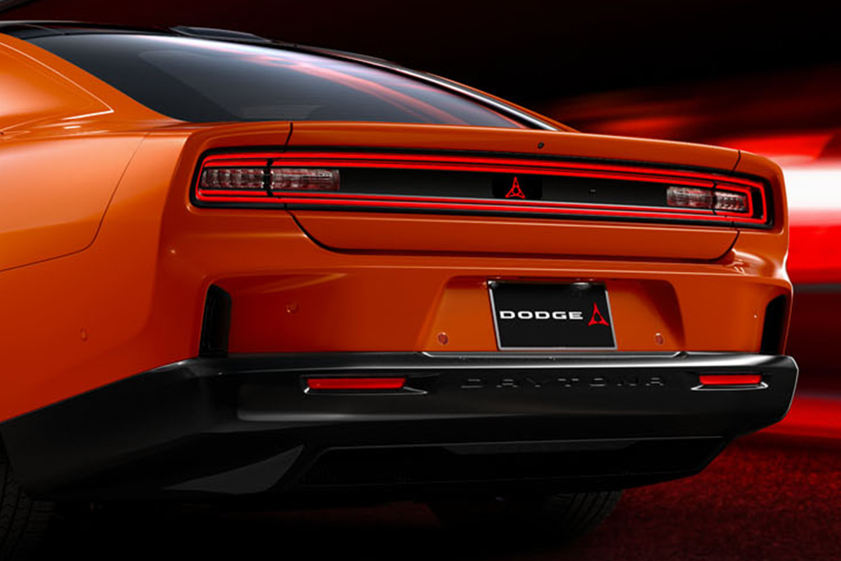 A back angled view of an orange Dodge Charger vehicle with blurry red lights shown in the distance.