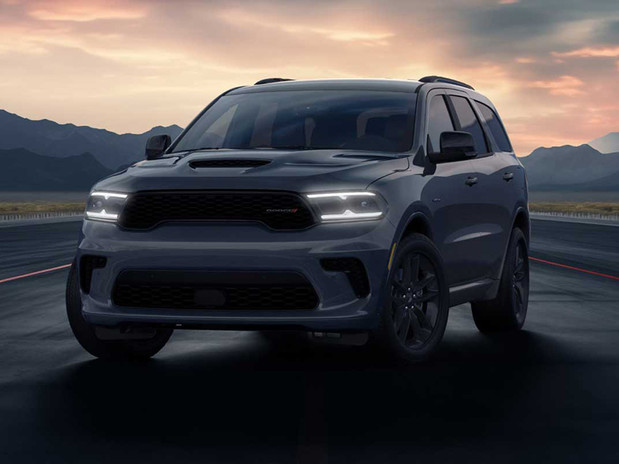 Vue de face d'un VUS Dodge Durango à 3 rangées de sièges, avec ses phares à DEL allumés, stationné sur une piste au crépuscule.