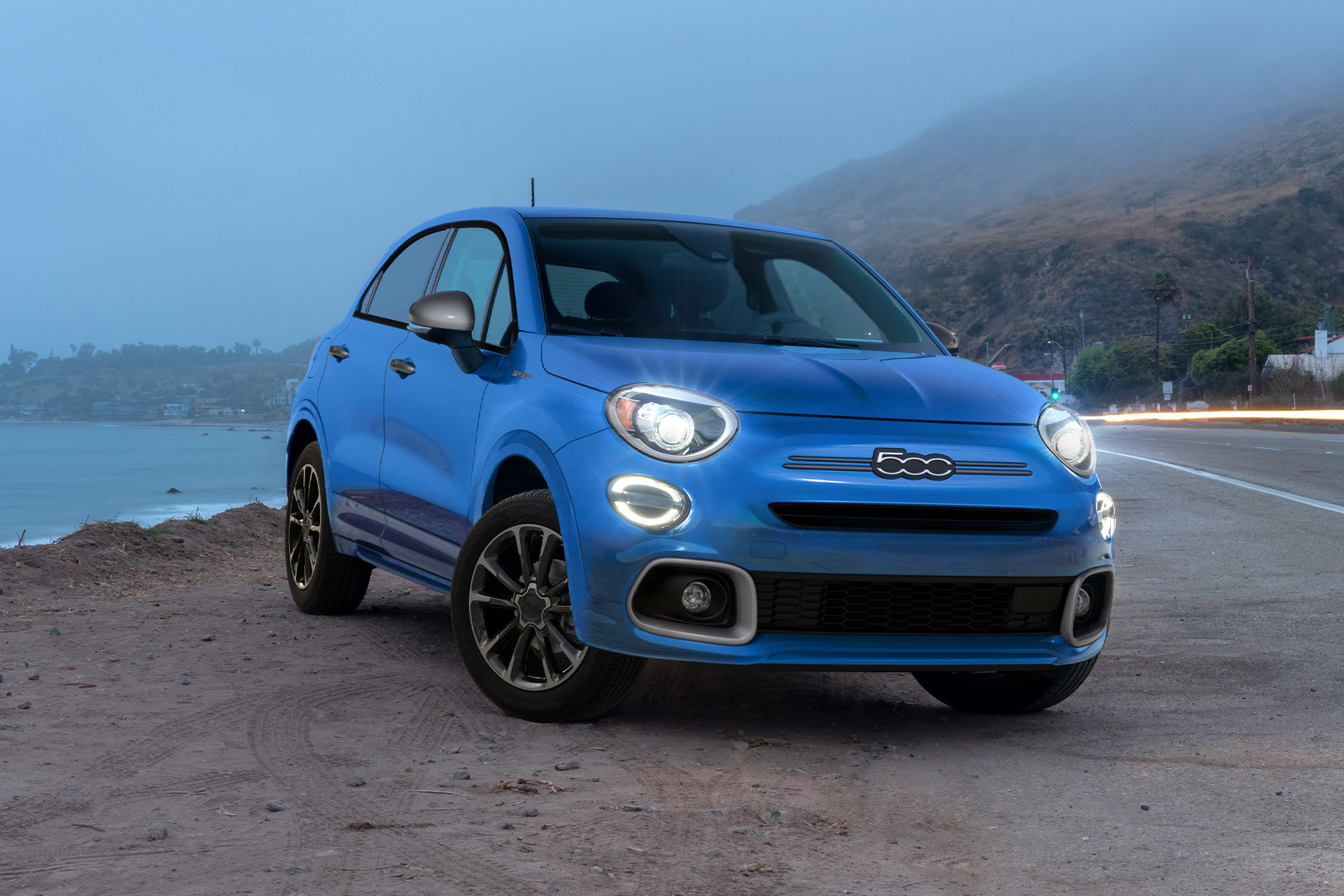 Passenger profile view of a blue 2023 Fiat 500X with headlamps and wheel trim displayed.