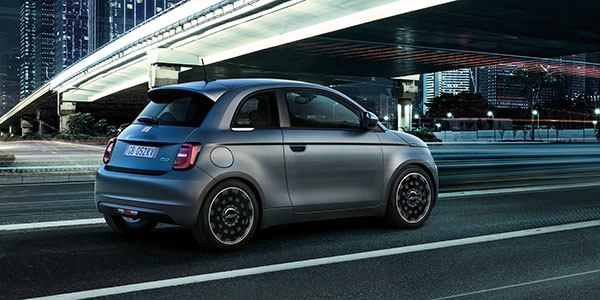 Side view of a 2024 Fiat 500e being driven in a city at night.