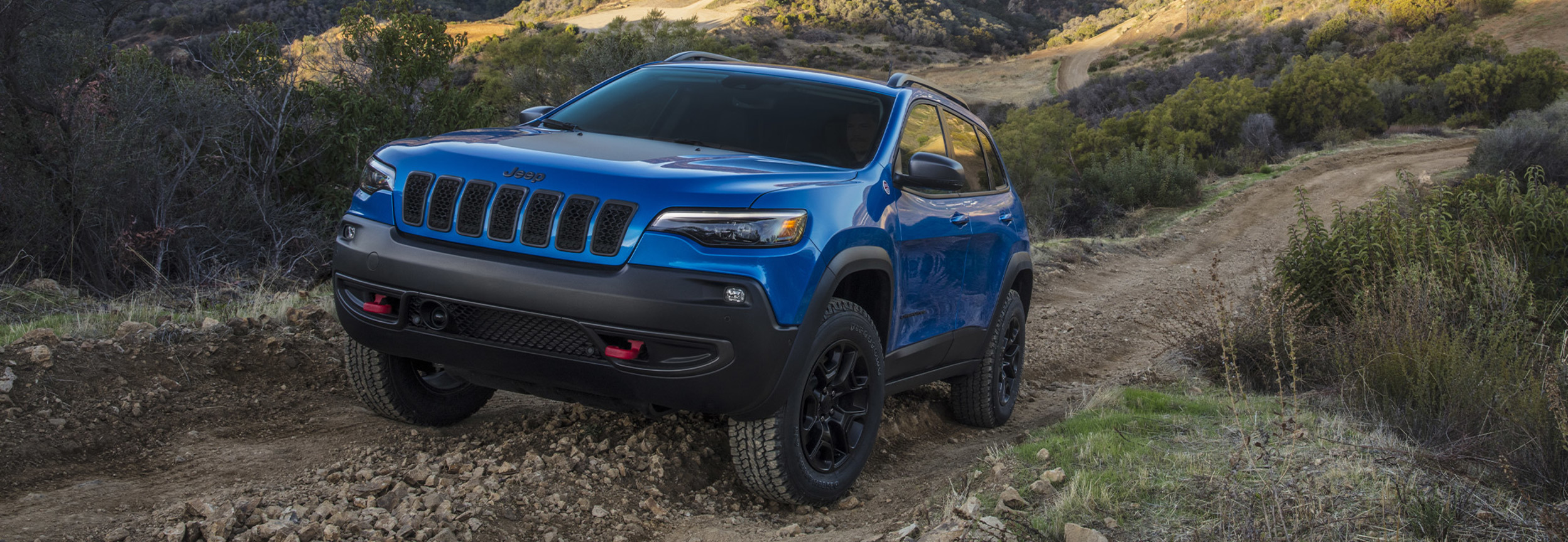 A 2022 Jeep Cherokee SUV  driving on a rocky off-road trail in an arid landscape. 
