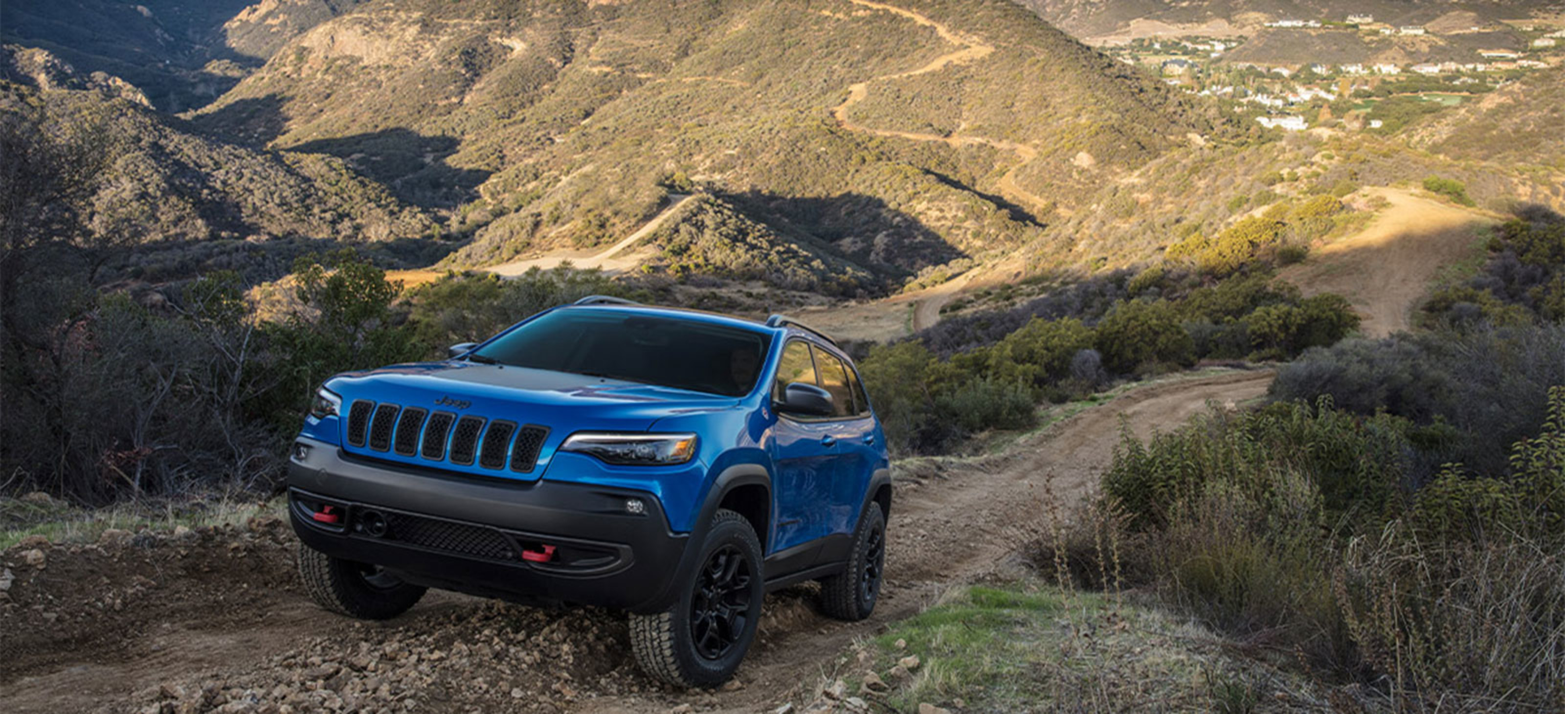 An angled view of a blue Cherokee being driven up a mountain. 