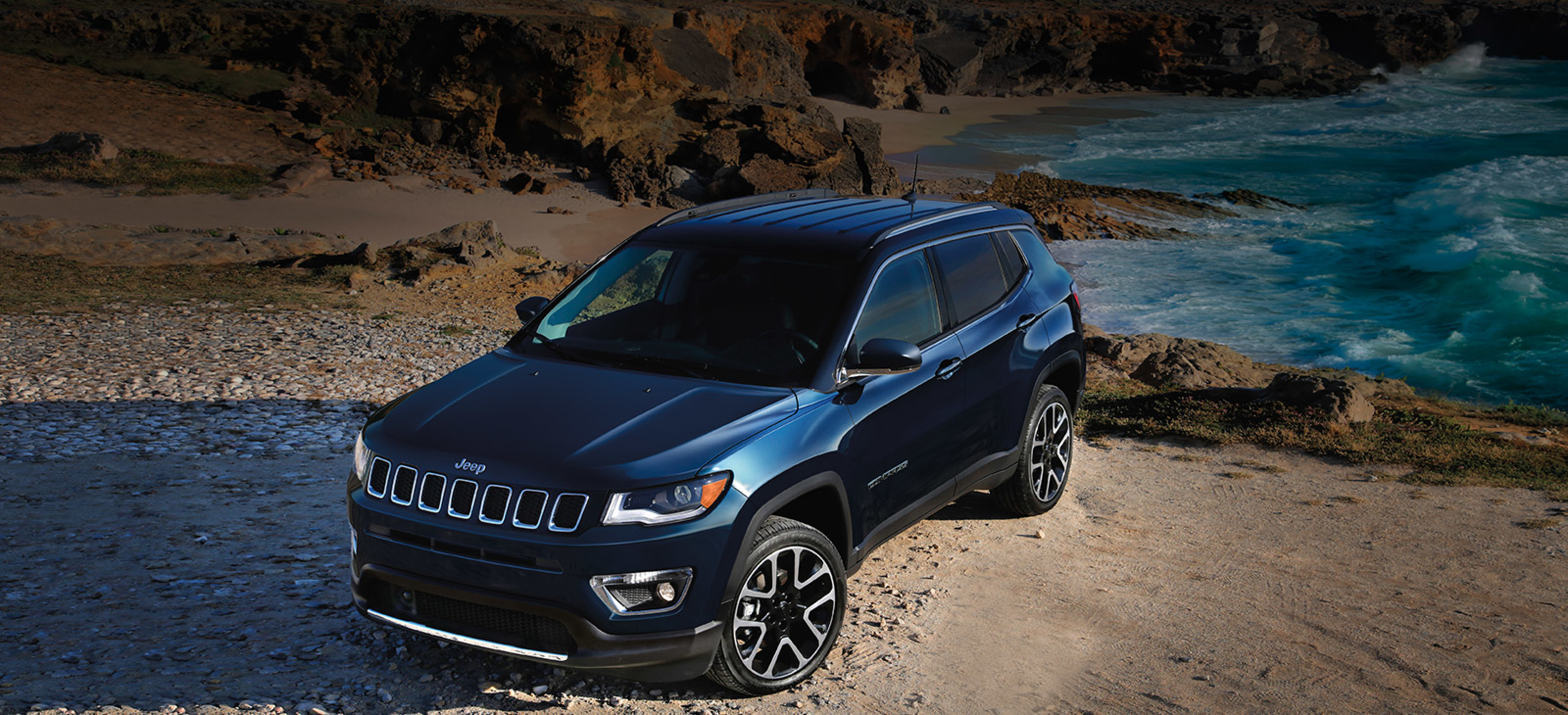 An overhead view of a Jazz Blue Pearl 2021 Jeep Compass parked on the beach with waves in the background.
