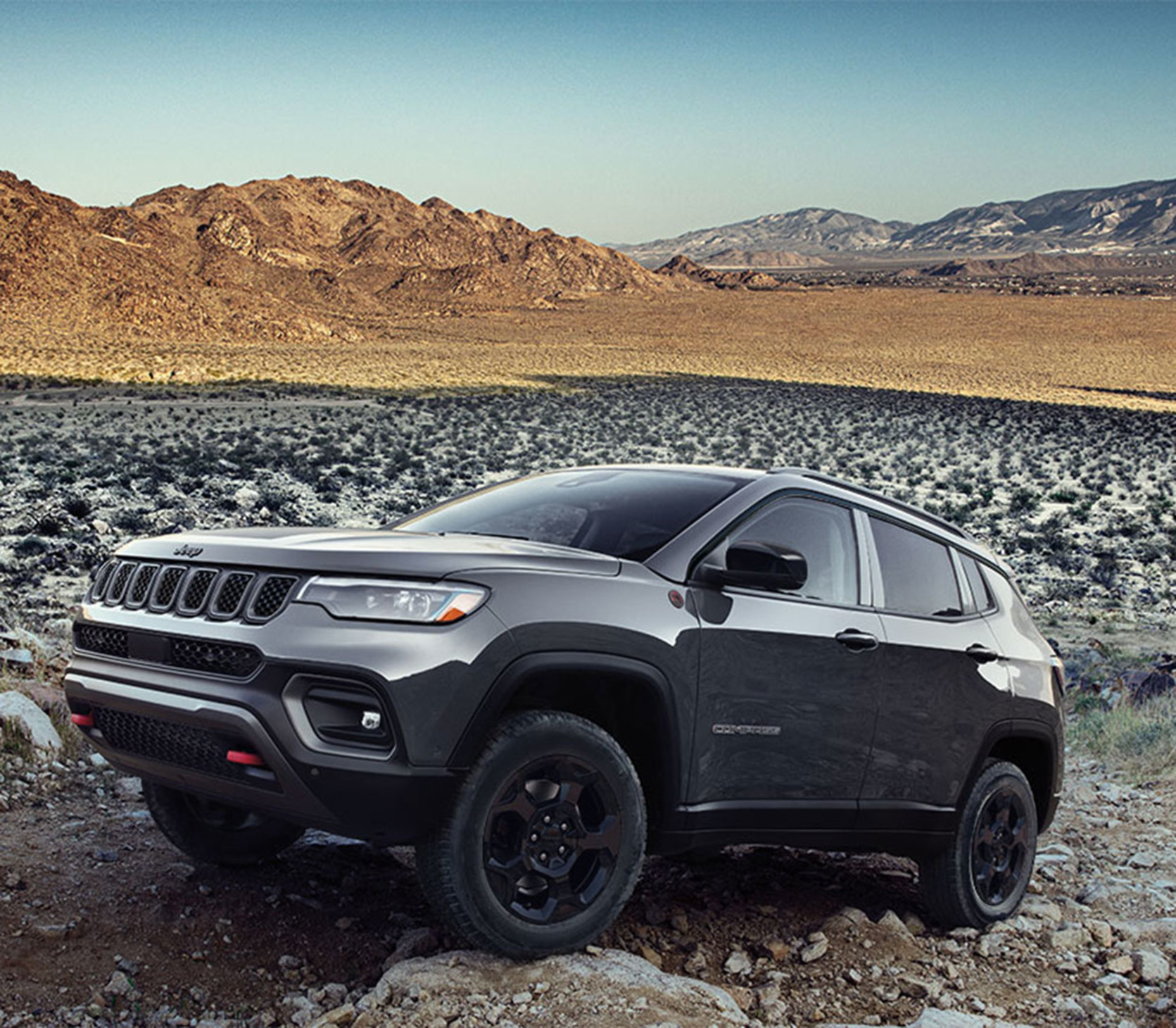 2023 Compass in dark grey parked on a gravel path with mountains in the background.