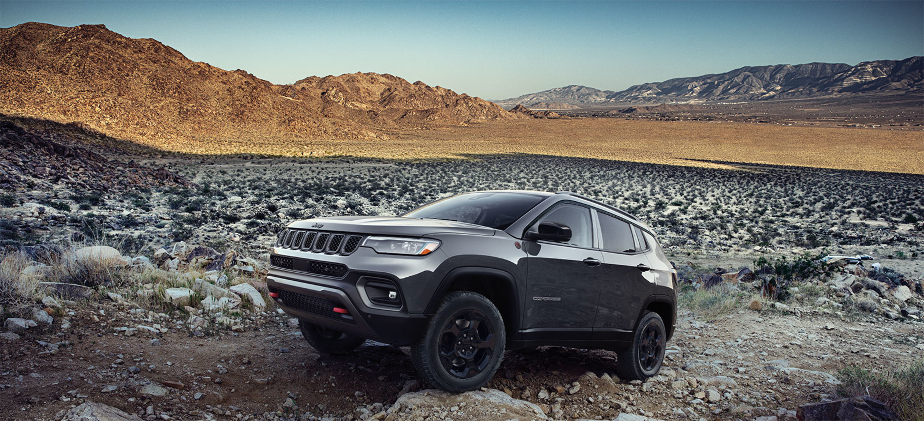 2023 Compass in dark grey parked on a gravel path with mountains in the background.