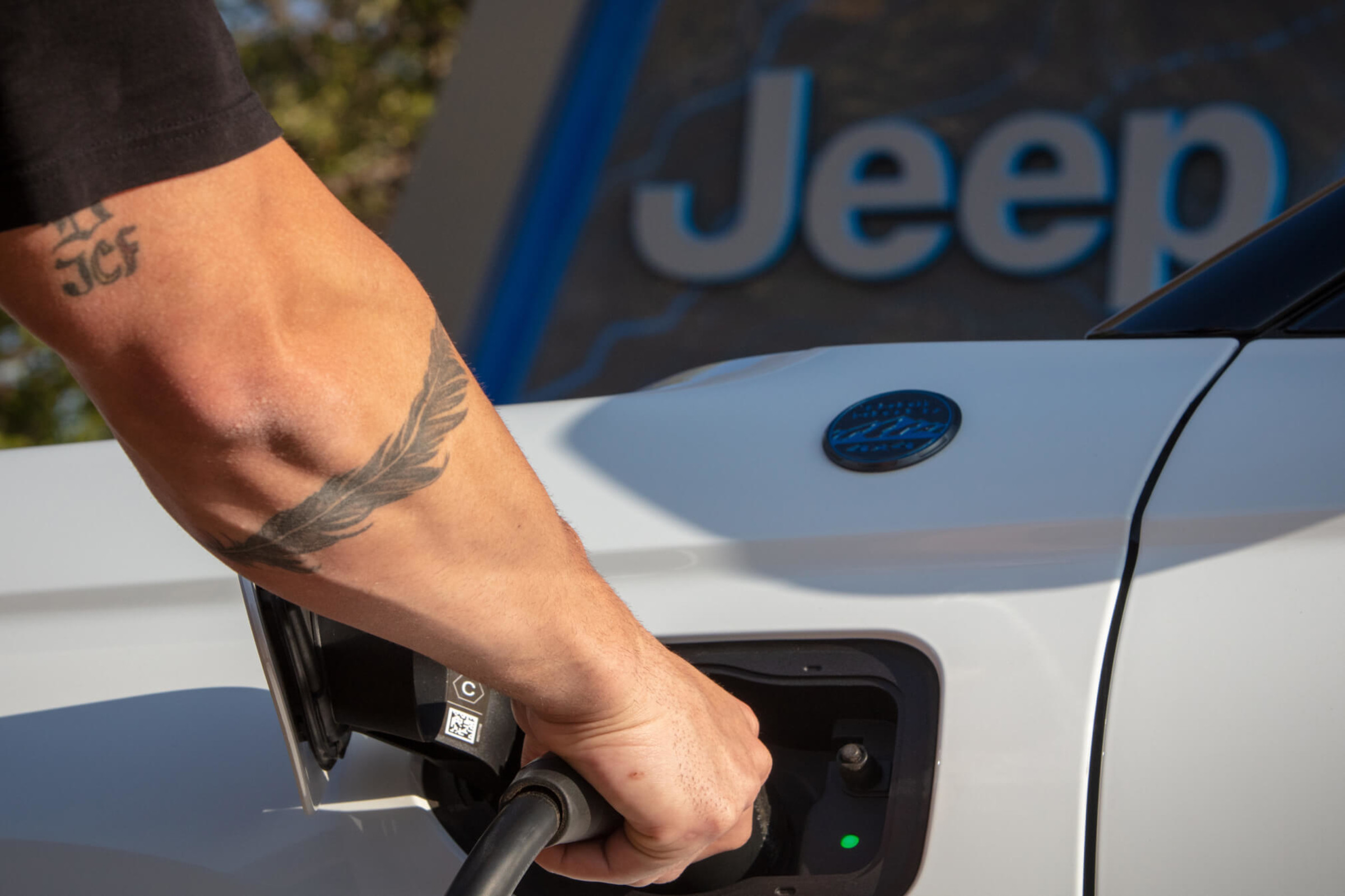 A close-up view of a person’s arm holding the charging cable while charging a white Jeep Grand Cherokee 4xe vehicle.