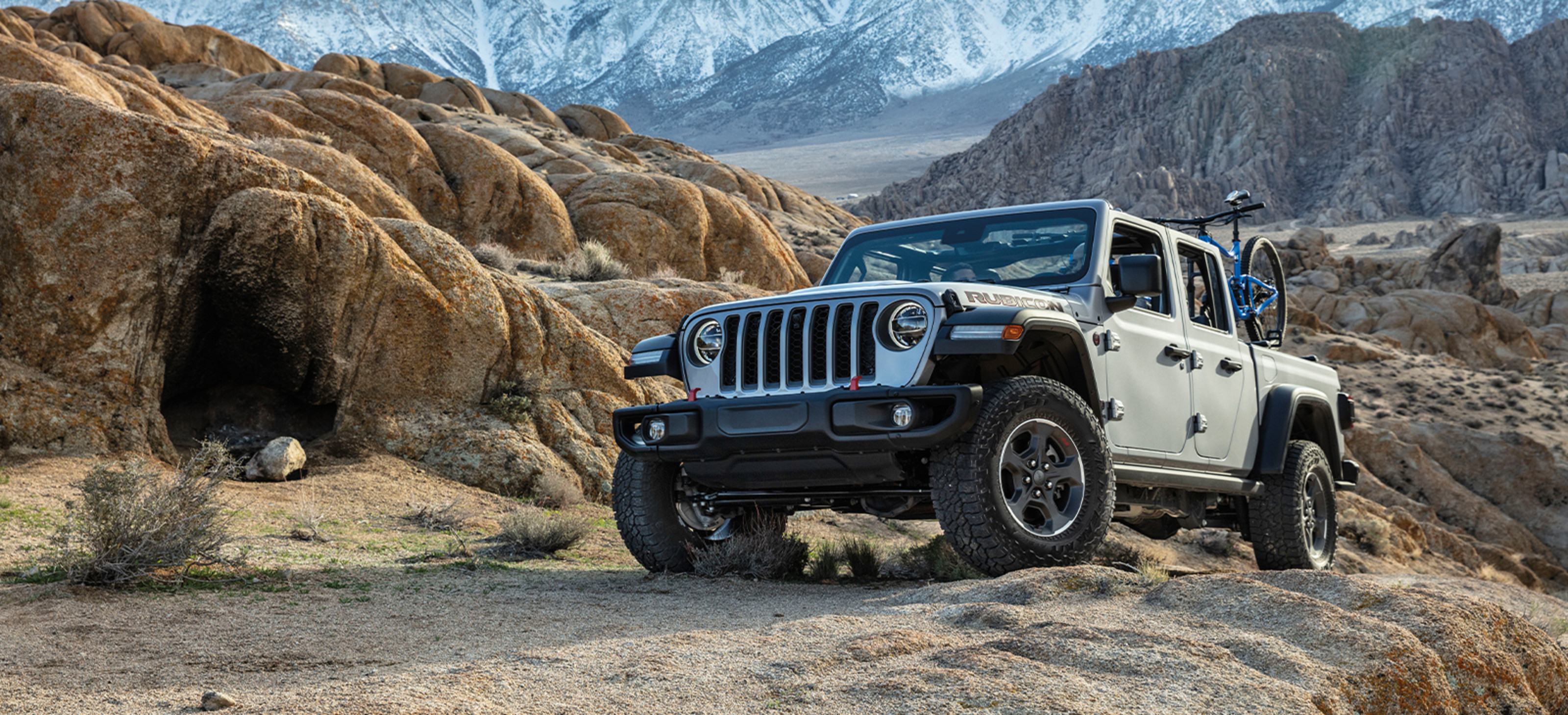 Un Jeep Gladiator 2022 gris clair garé sur un terrain rocailleux.