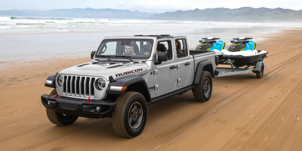 Un Jeep Gladiator 2023 gris remorquant un bateau sur une plage.