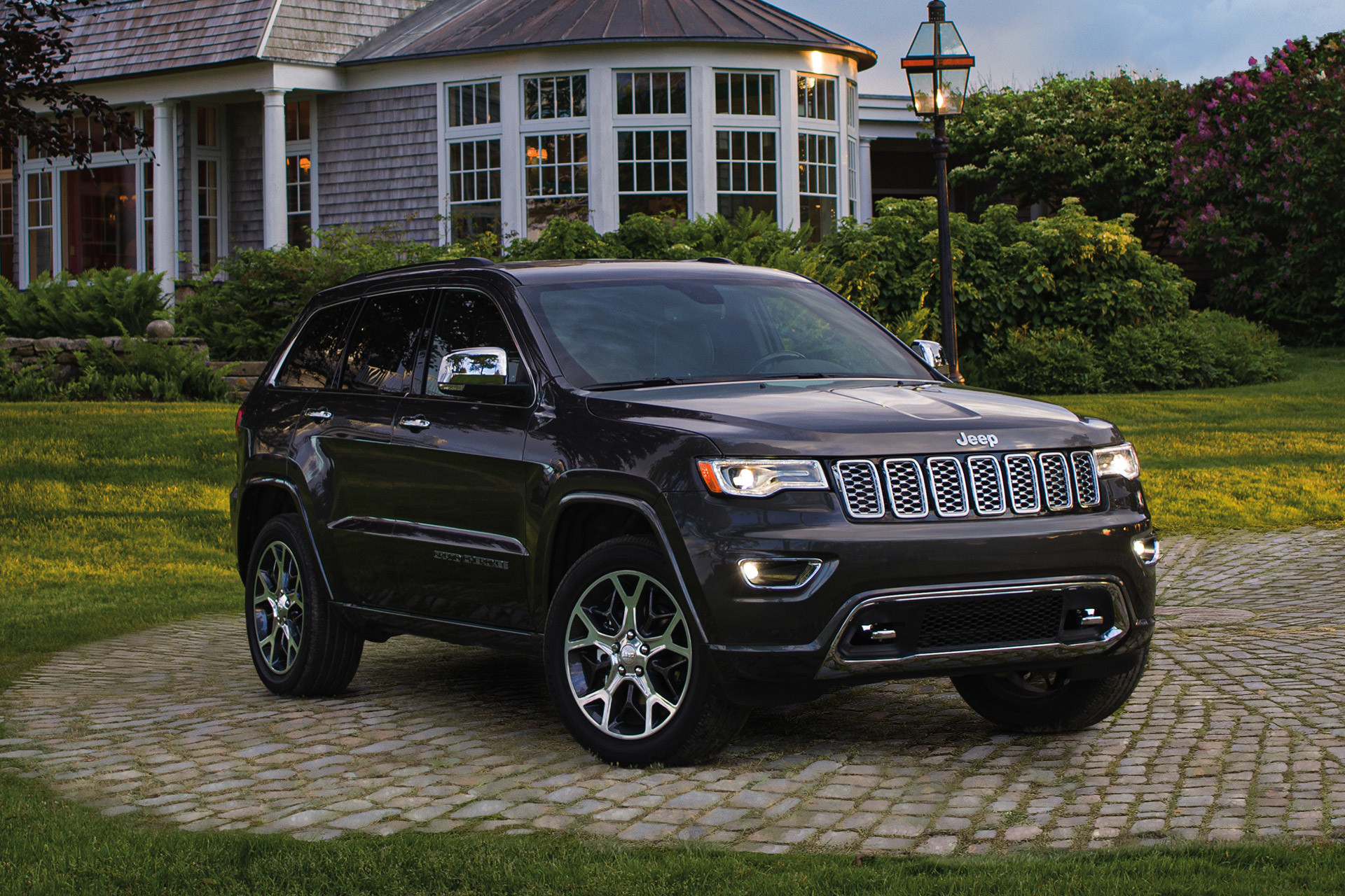 Navy blue Jeep Grand Cherokee parked in front of a large house surrounded by shrubs and grass. 