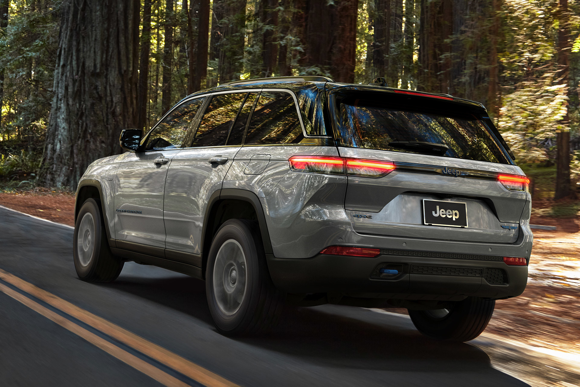 Rear view of a silver All-New 2022 Jeep Grand Cherokee 4xe being driven down a forest road.