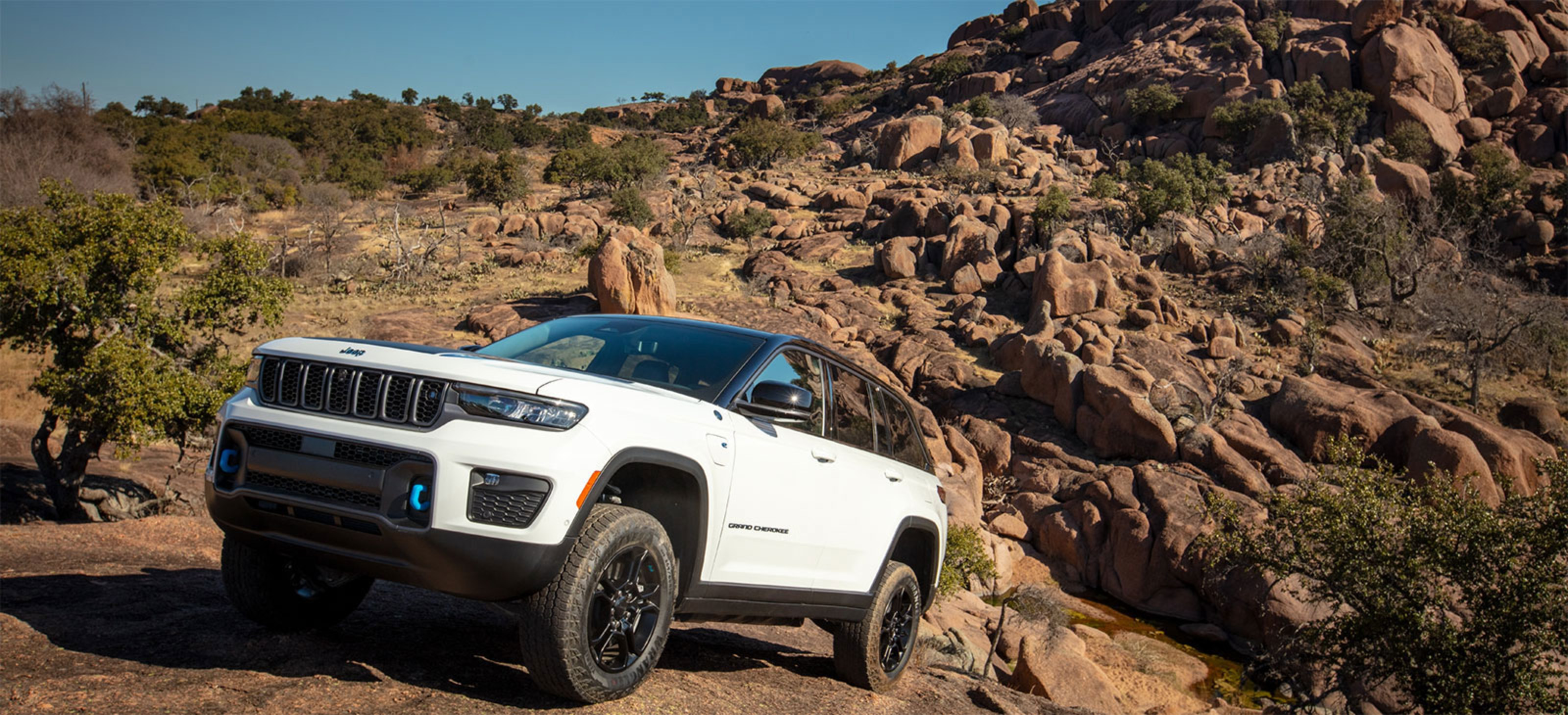 A white 2023 Jeep Grand Cherokee 4xe parked on top of a hill with mountainous vista behind it.
