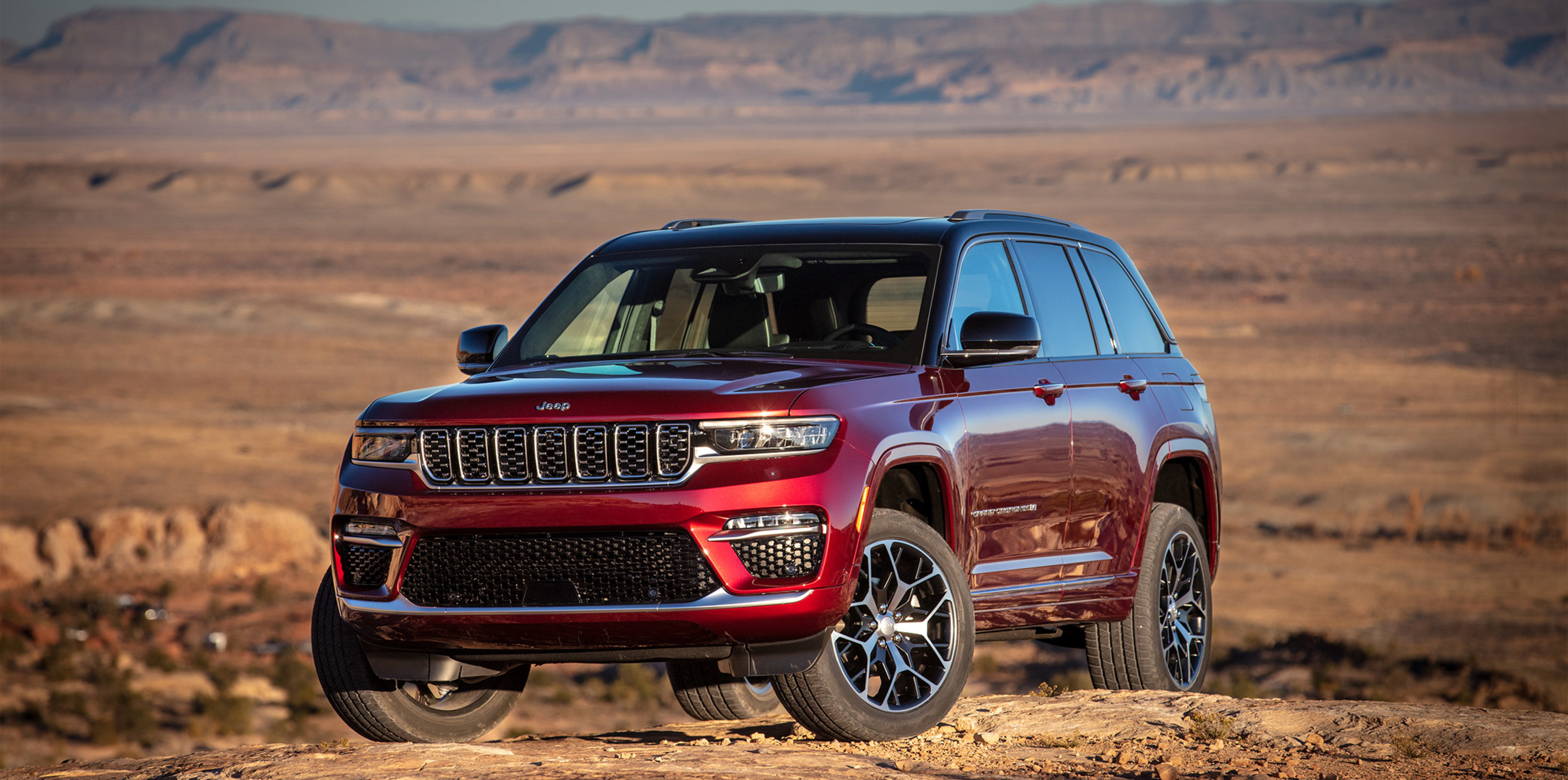 Red 2023 Jeep Grand Cherokee parked on top of a hill against a desert backdrop.