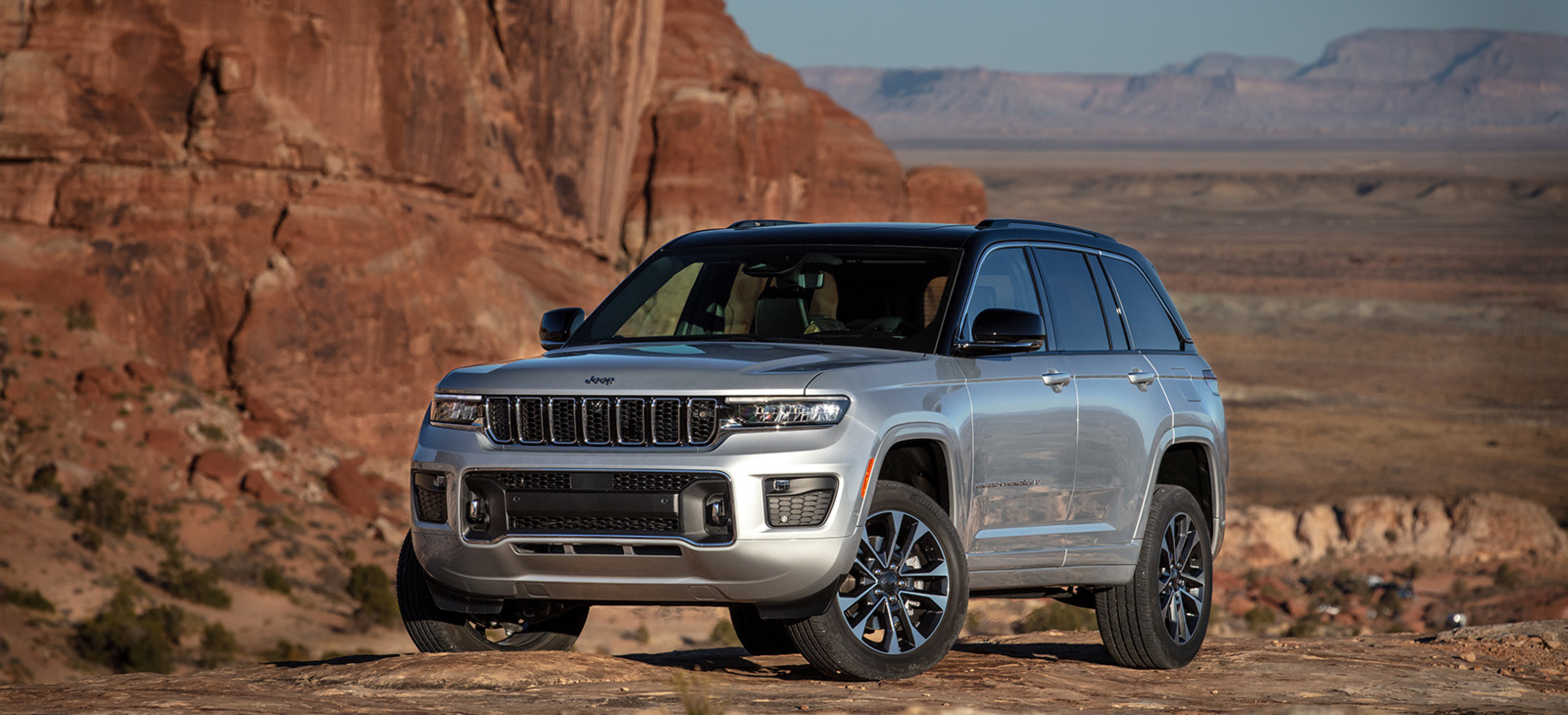 View of a silver 2024 Jeep Grand Cherokee shown parked on desert terrain.