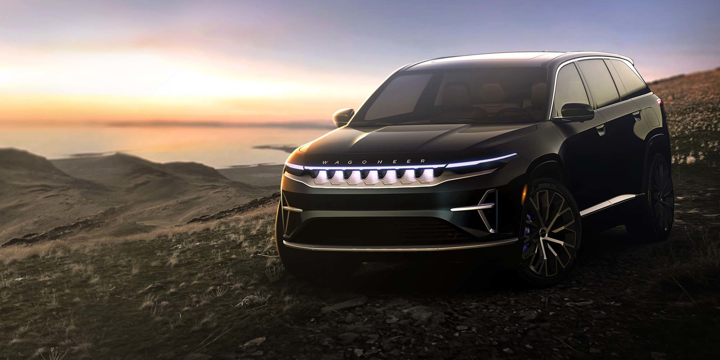 View of a black Wagoneer EV model parked on top of a hill with a body of water in the background.