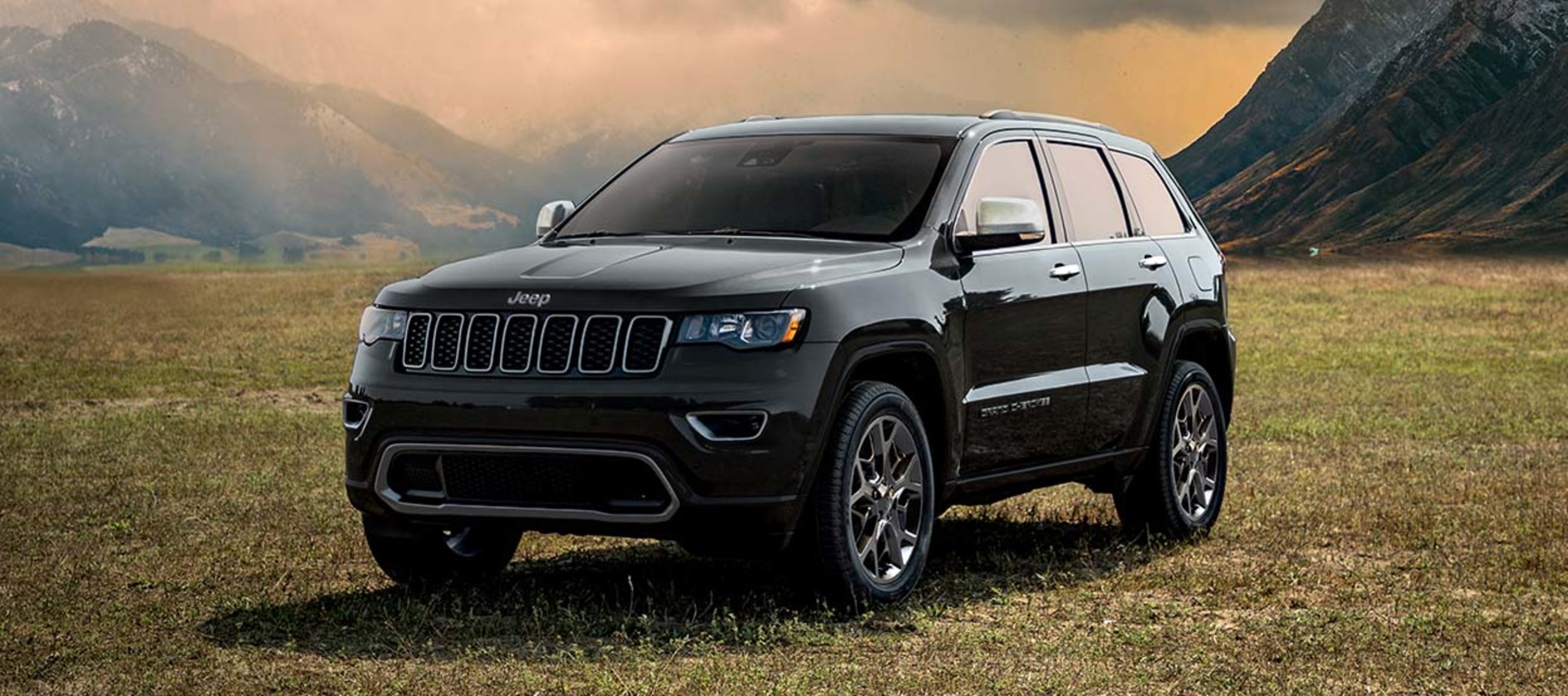 A grey 2022 Grand Cherokee WK parked in an open grass field with mountains in the background