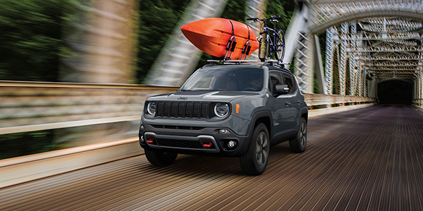 A grey  2022 Jeep Renegade driving down a bridge with a canoe strapped to the roof 