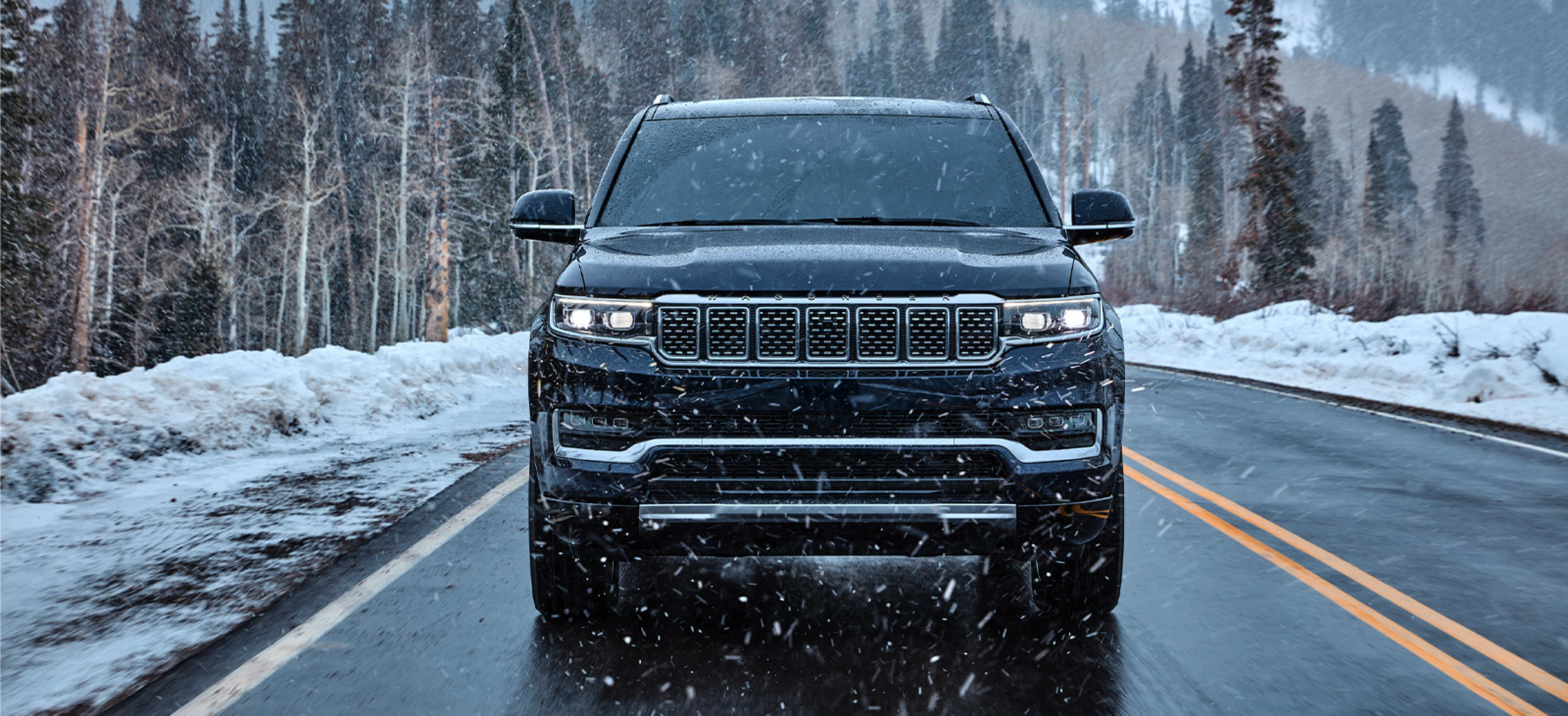 Front view of a 2022 black Grand Wagoneer, being driven on a snowy road in the moutains
