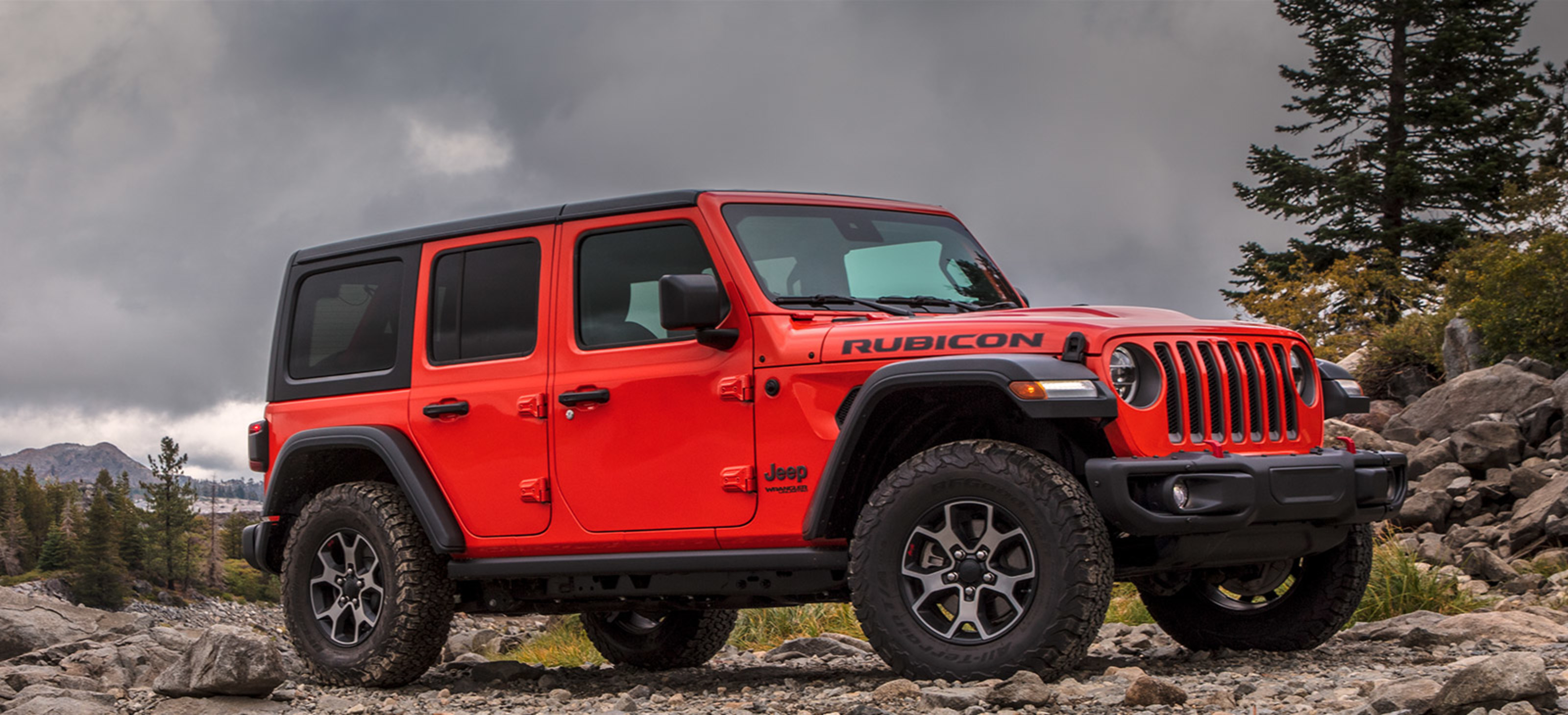 A side view of a four-door Firecracker Red 2021 Jeep Wrangler Rubicon parked on rocky terrain in the wilderness.
