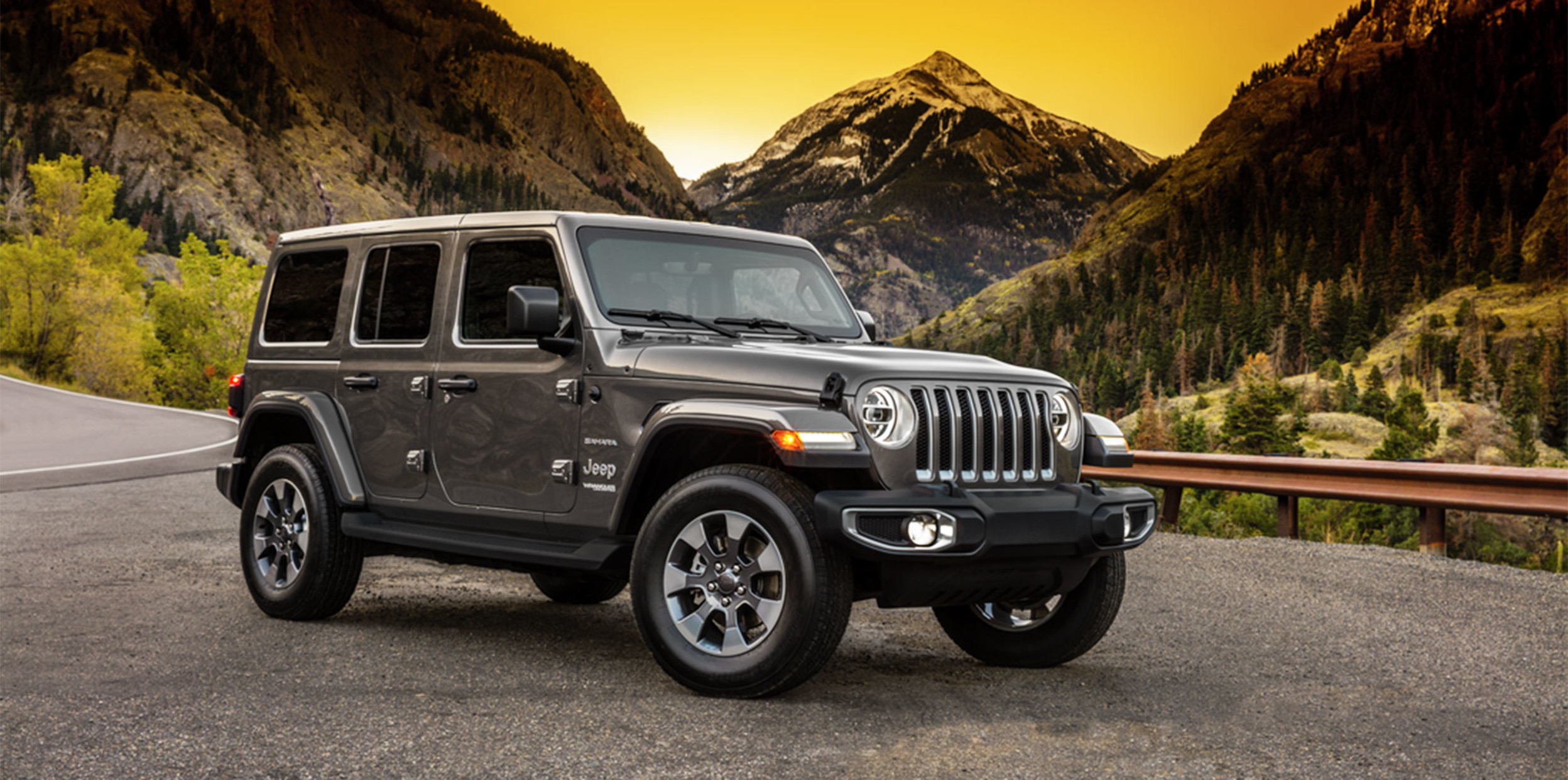 Black Jeep Wrangler parked on road with mountains in the background.