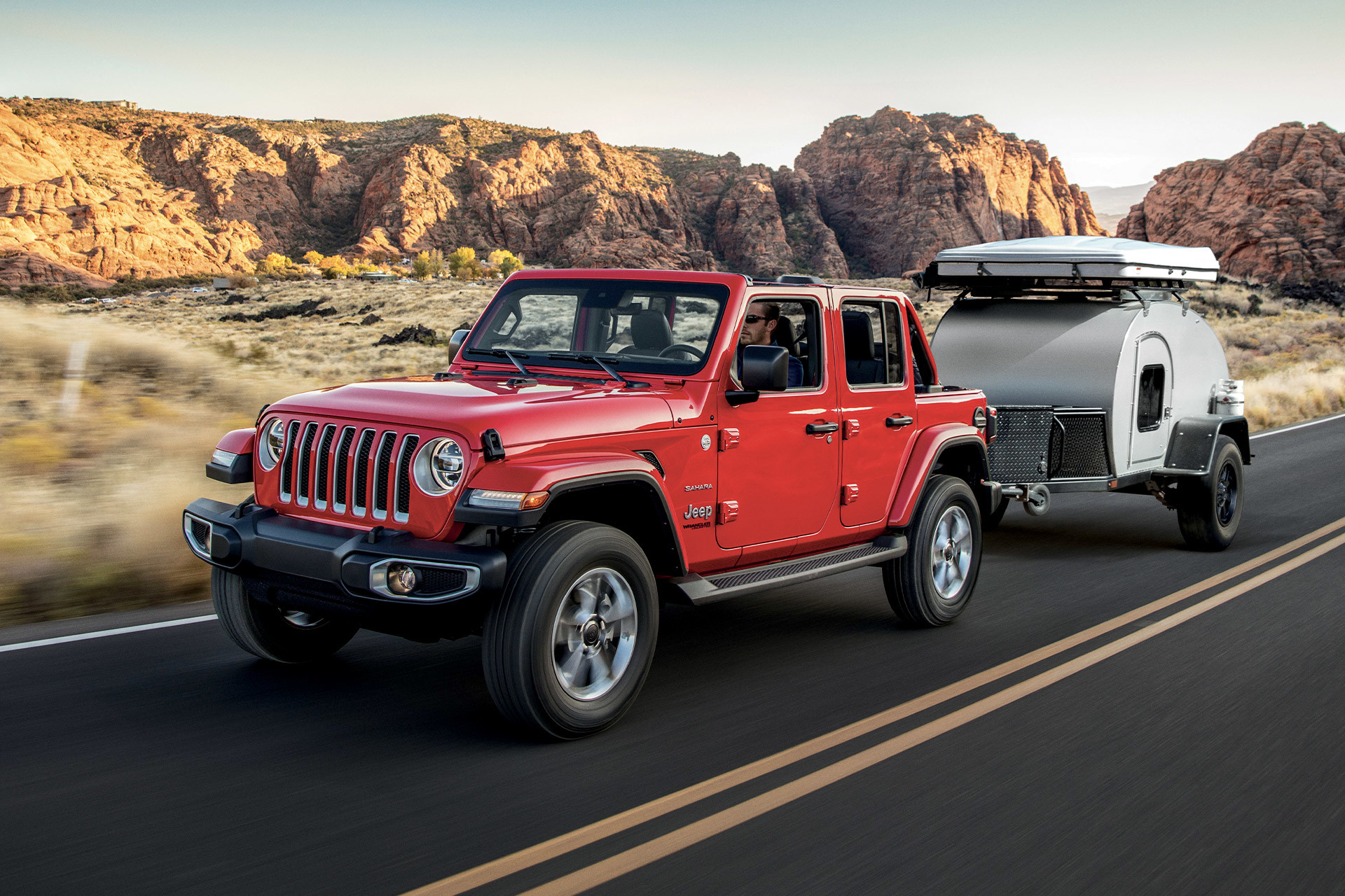 Red 2022 Jeep Wrangler towing a mini camper with a desert background