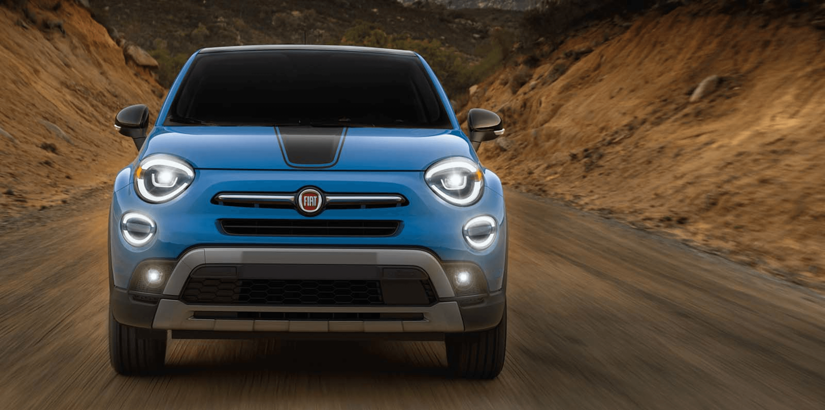 The front of a blue Fiat 500X driving on a dirt road.