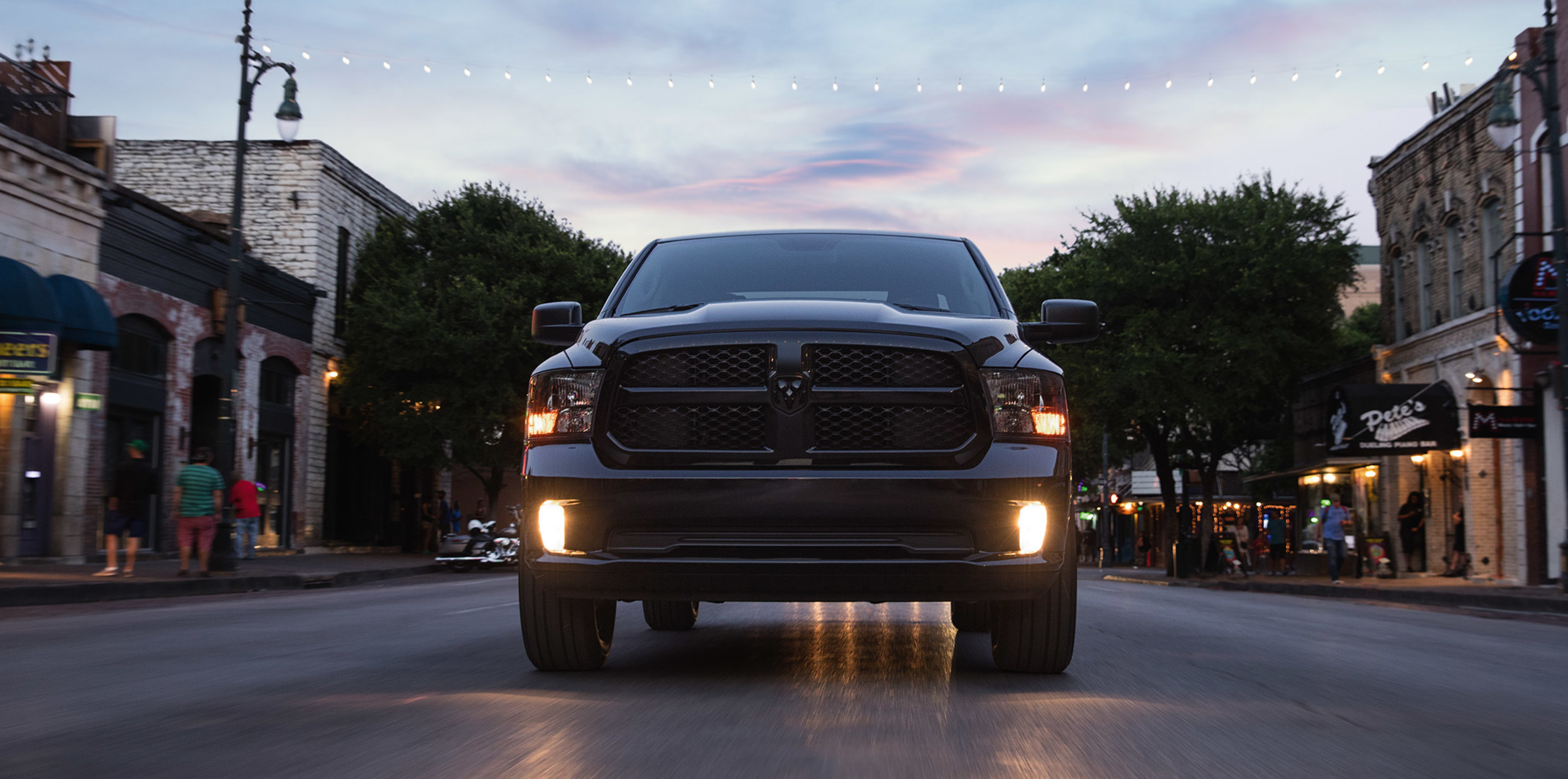 Front view of Ram 1500 Classic with lights on driving on street.