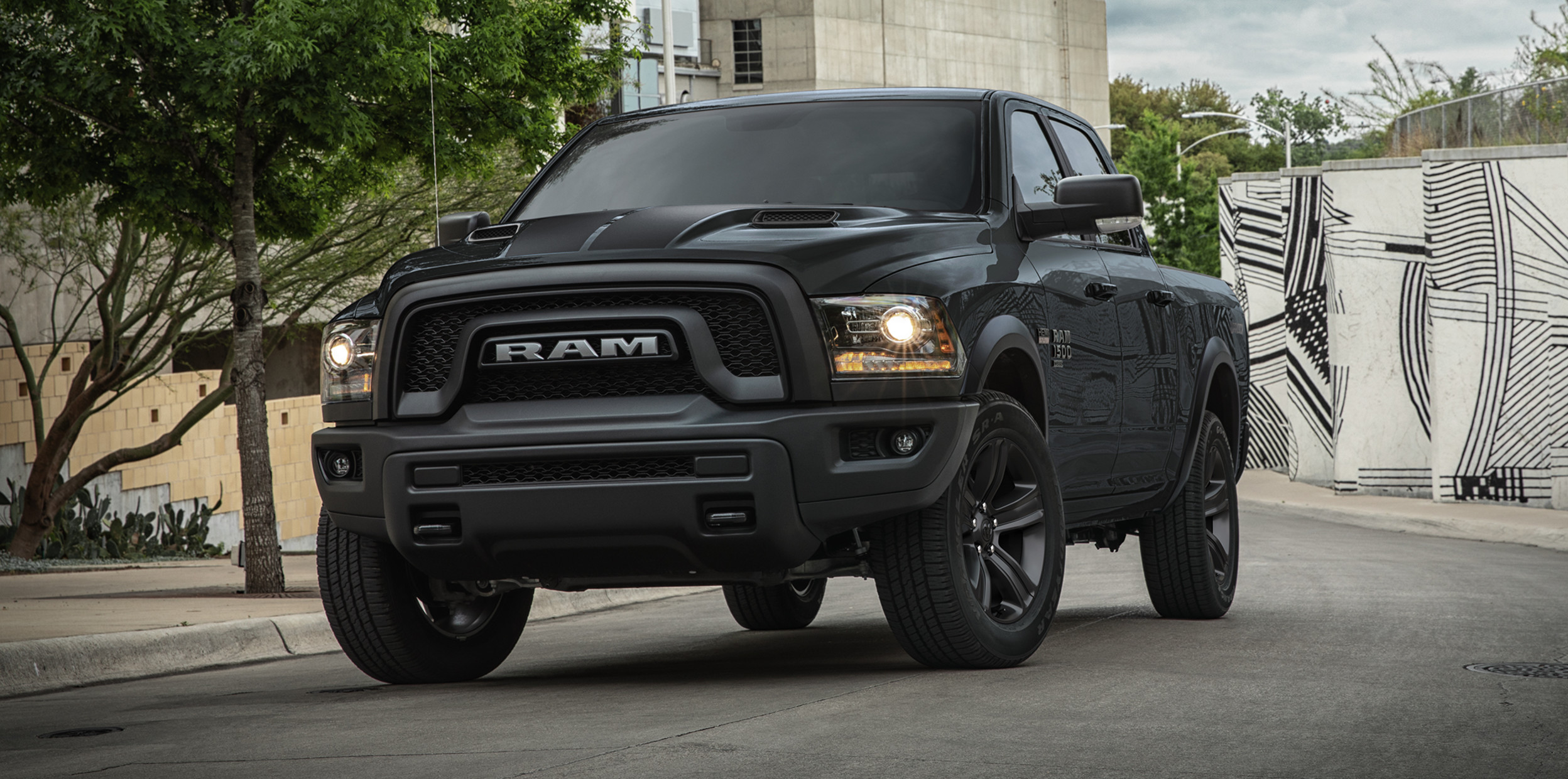 A black 2022 Ram 1500 Classic, being driven on a paved road with buildings and trees in the background.