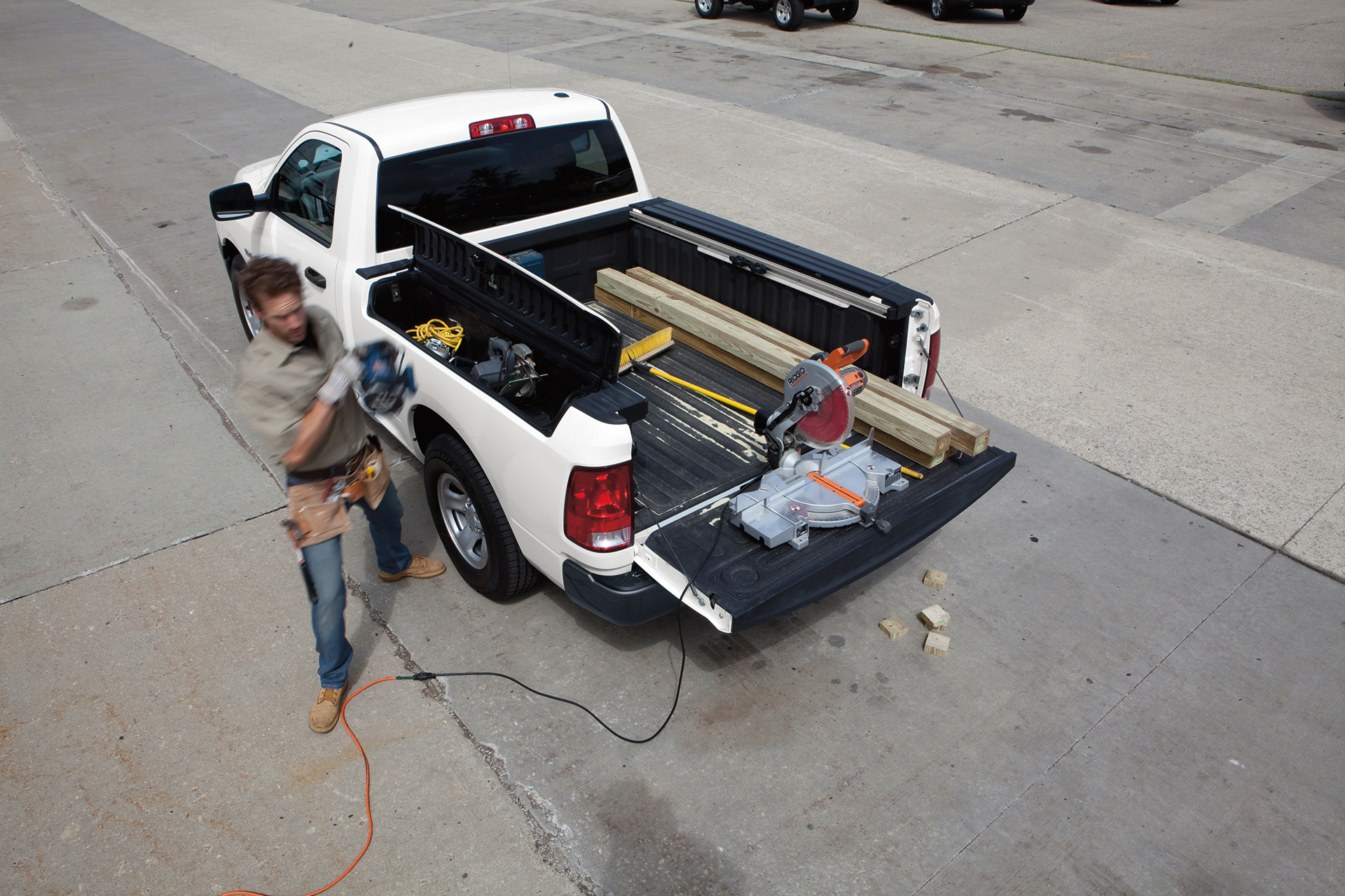 A person loading a white 2022 Ram 1500 Classic with various tools and materials.