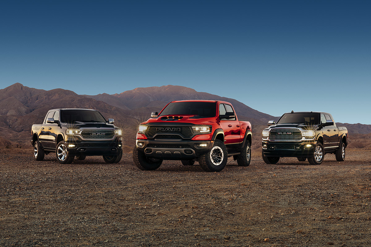 Ram 1500, Ram 1500 TRX and Ram 2500 are parked side-by-side on a desert plain with bare mountains and dark blue sky in the background. Over the past three years,  each vehicle has had its turn to win MotorTrend Truck of the Year. 