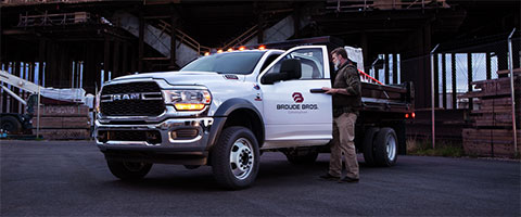 A front angled view of a white 2024 Ram Chassis Cab with the driver door being opened by a man with a bridge shown in the distance.